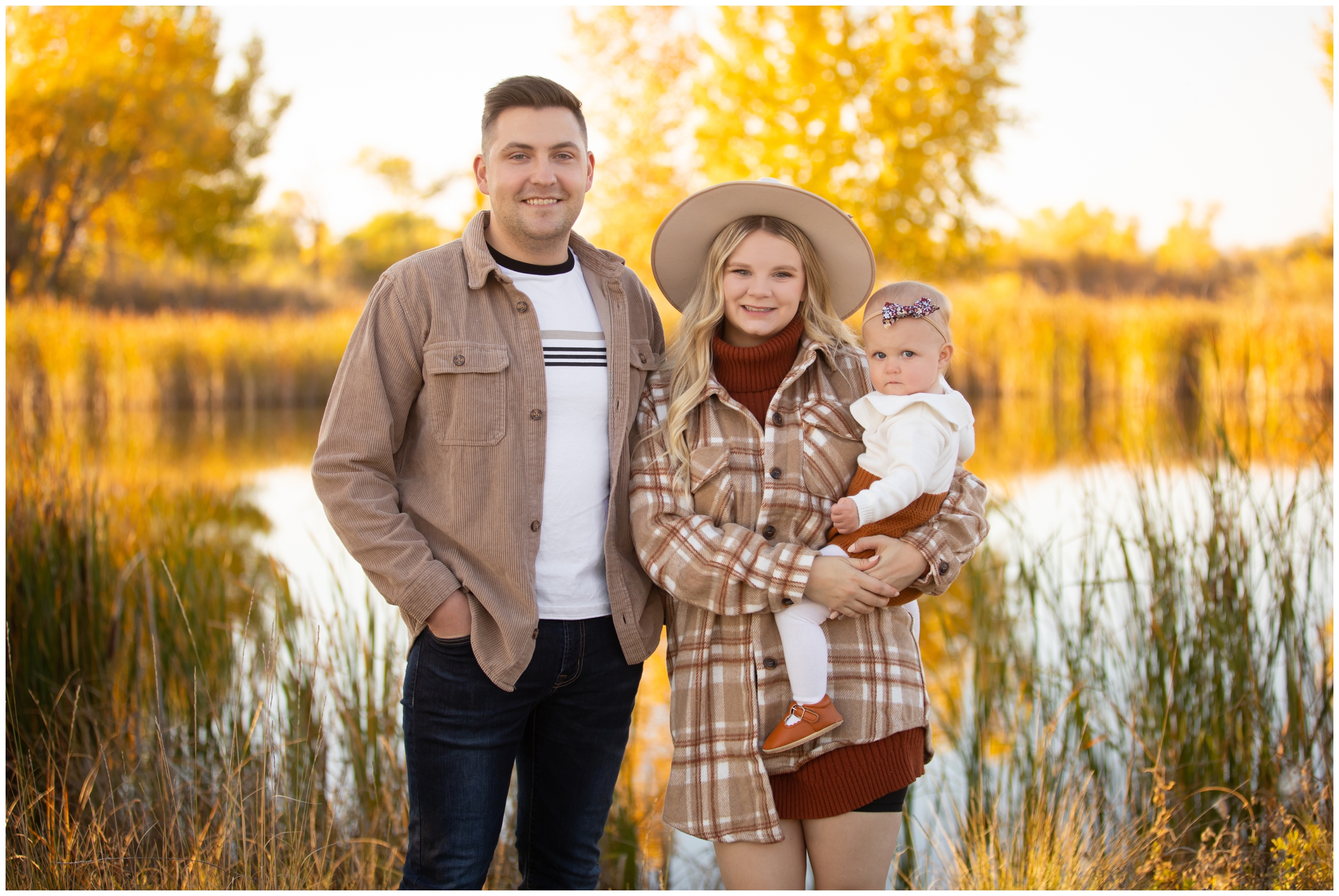 family posing next to pond with fall foliage in background during Longmont family photography session
