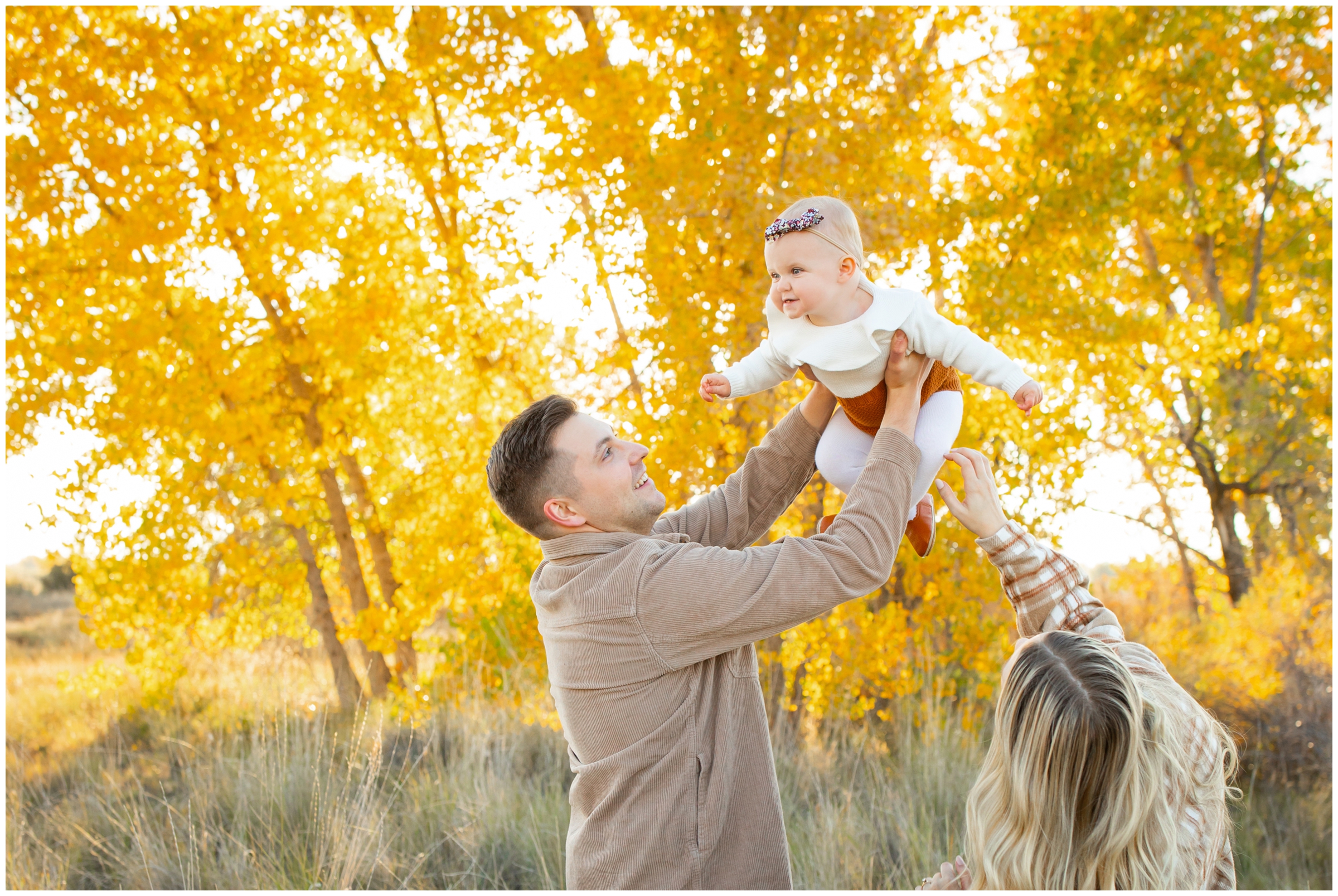 dad lifting baby daughter into the air during fall family portraits at Idaho Creek in Longmont Colorado 