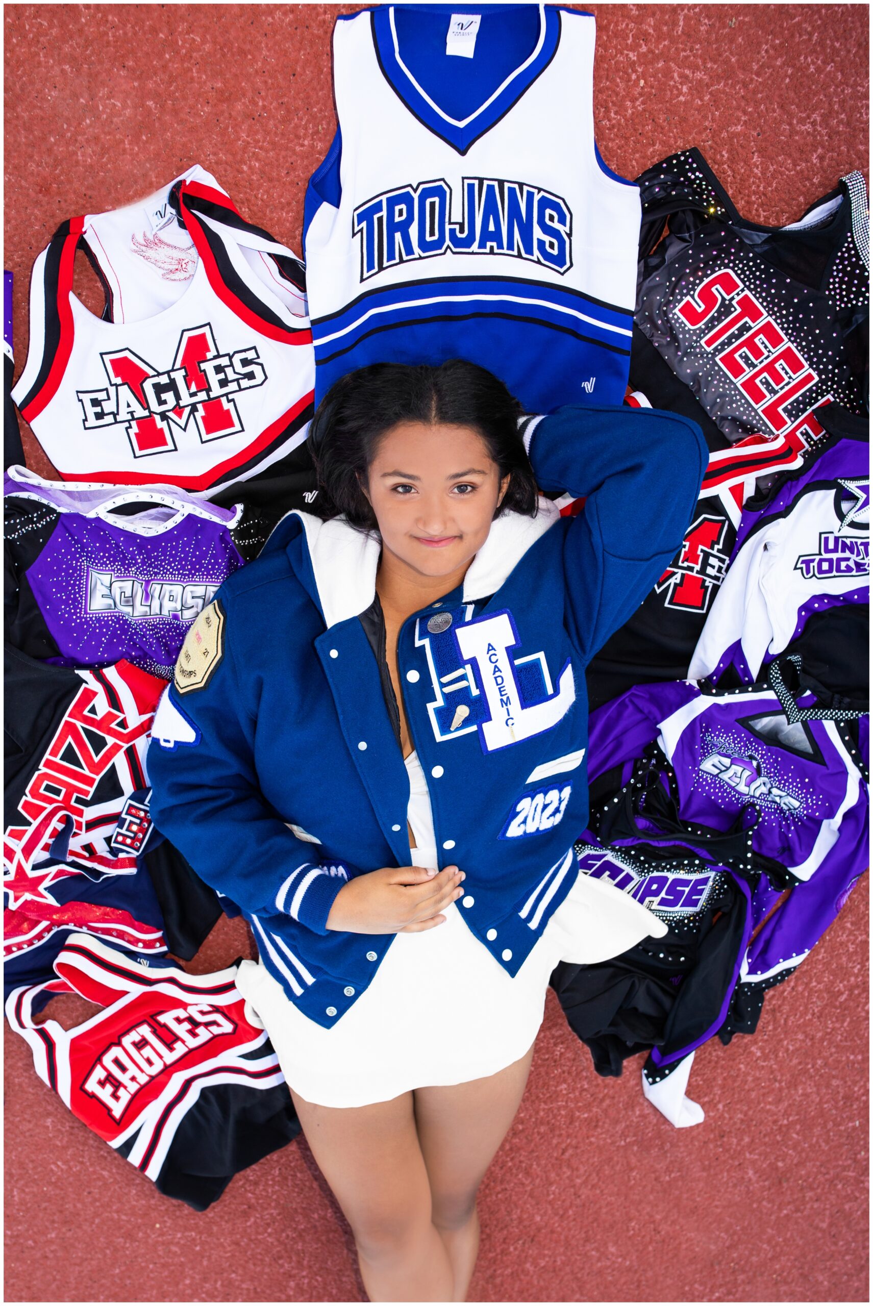 teen laying on all her old cheerleading uniforms during Longmont Colorado senior photography session