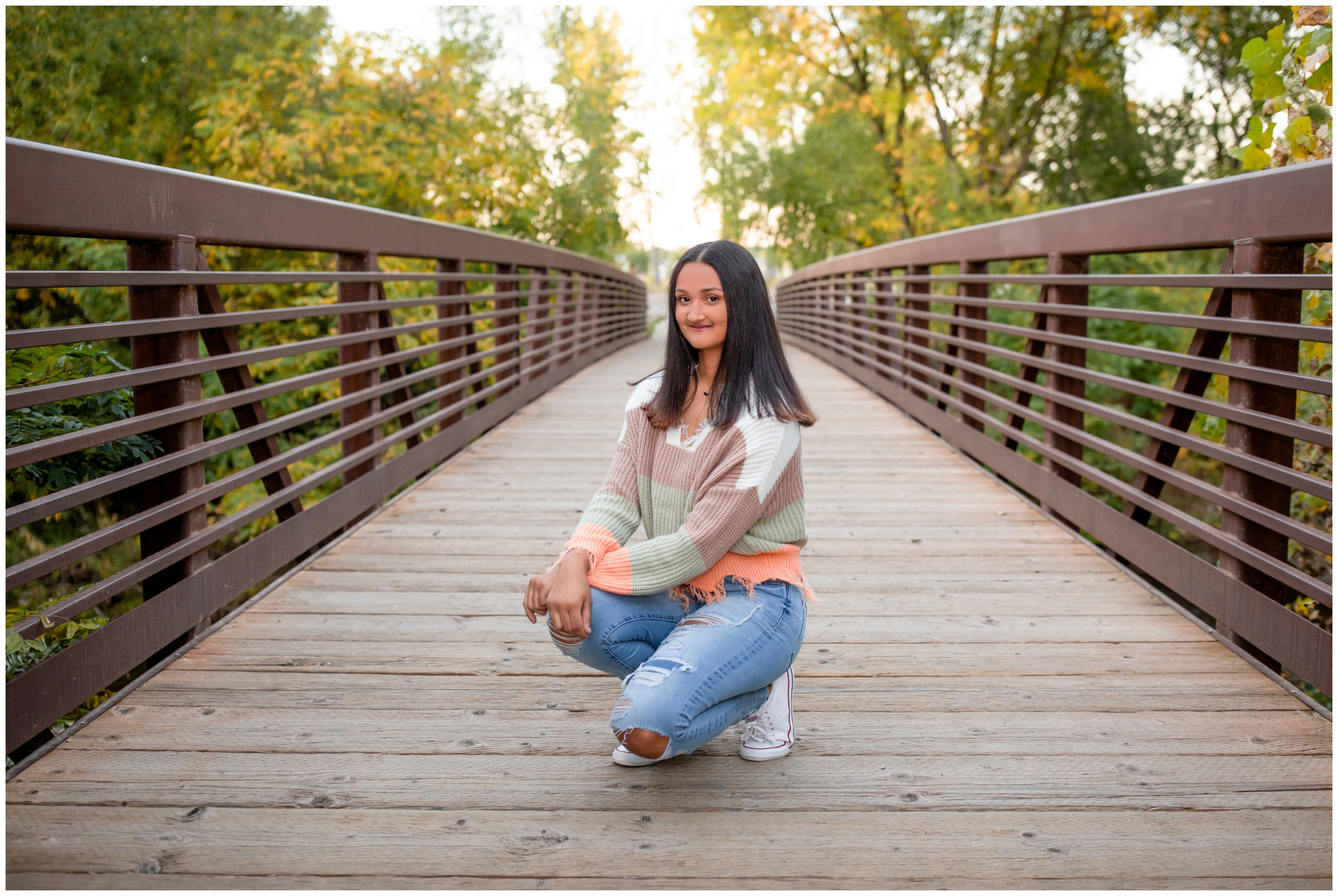 teen squatting on bridge during fall senior pictures  at Golden Ponds Longmont 