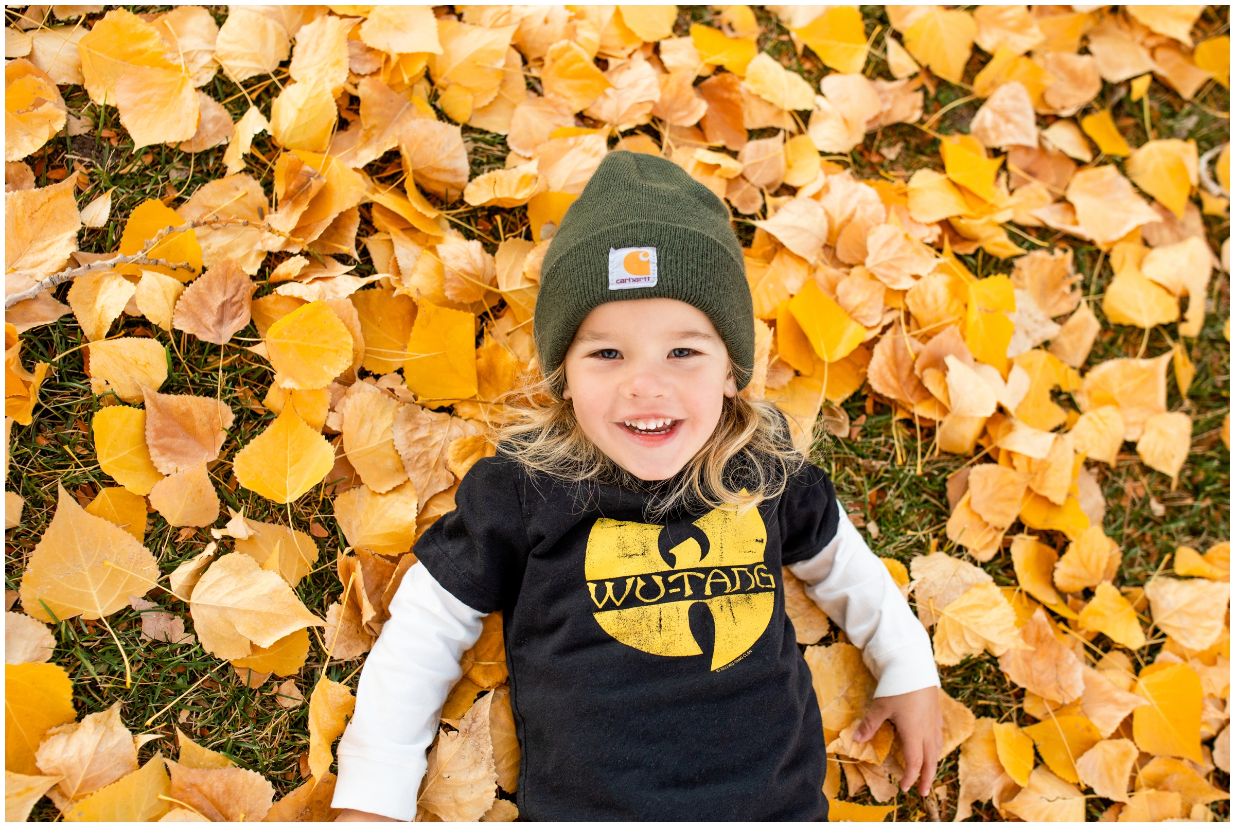 little boy laying in pile of leaves during fall family portraits in Lyons Colorado 