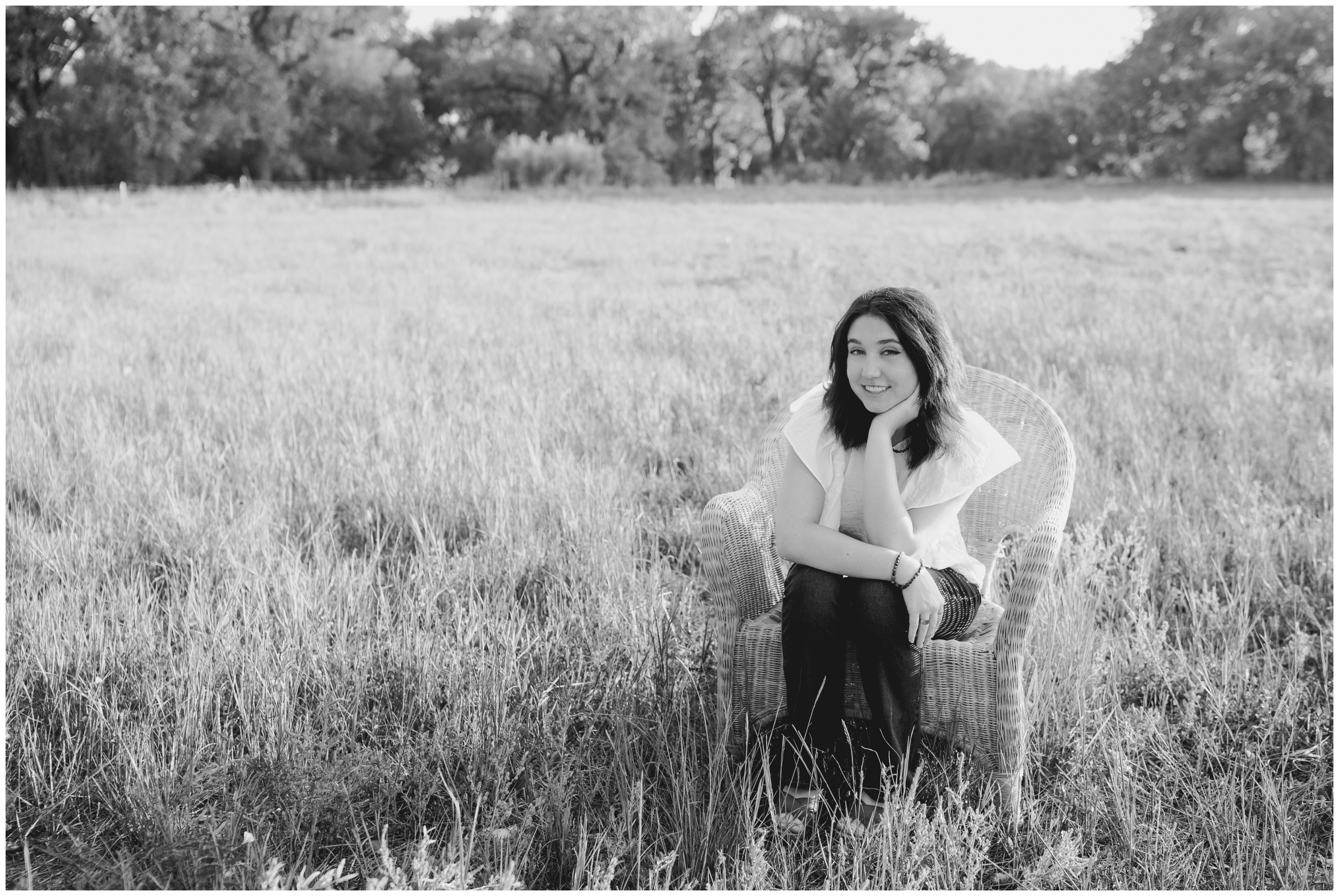 teen sitting on a wicker chair in a field during high school graduation portraits in Longmont