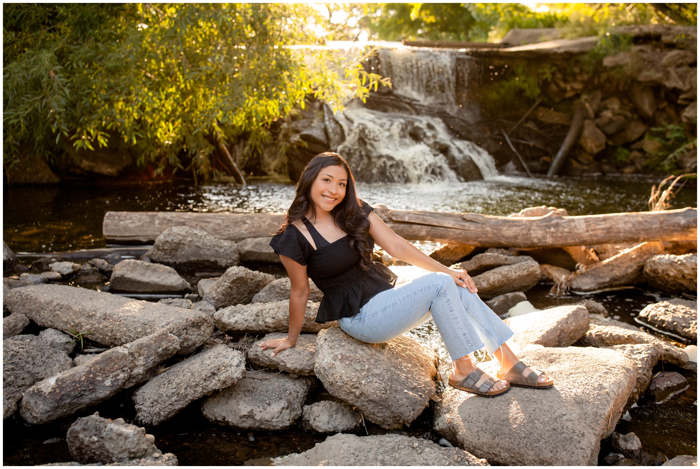 teen girl sitting on rocks near a waterfall during Colorado senior photography session at Golden Ponds