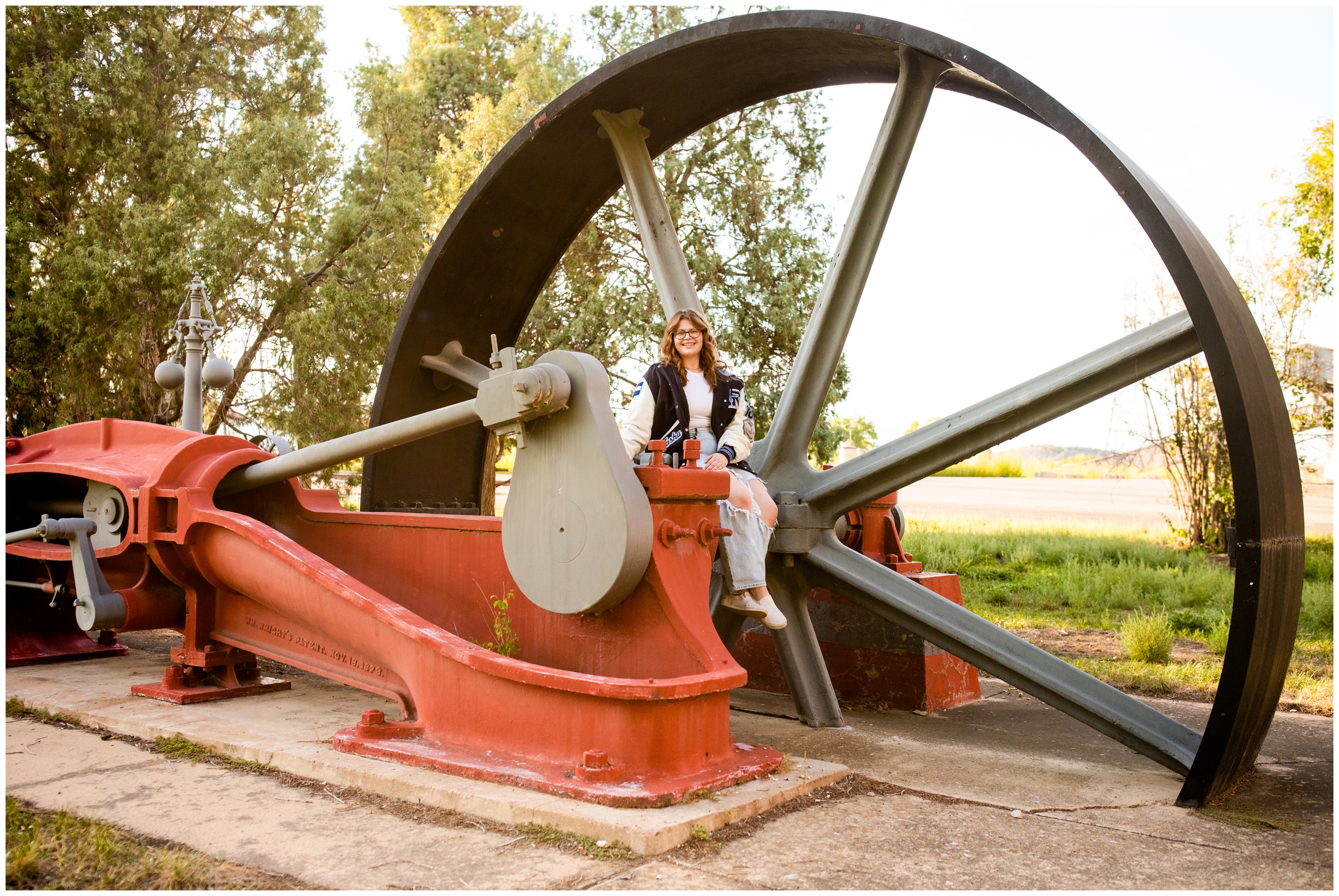 teen girl sitting on old compound steam engine during unique Colorado senior pictures in Boulder