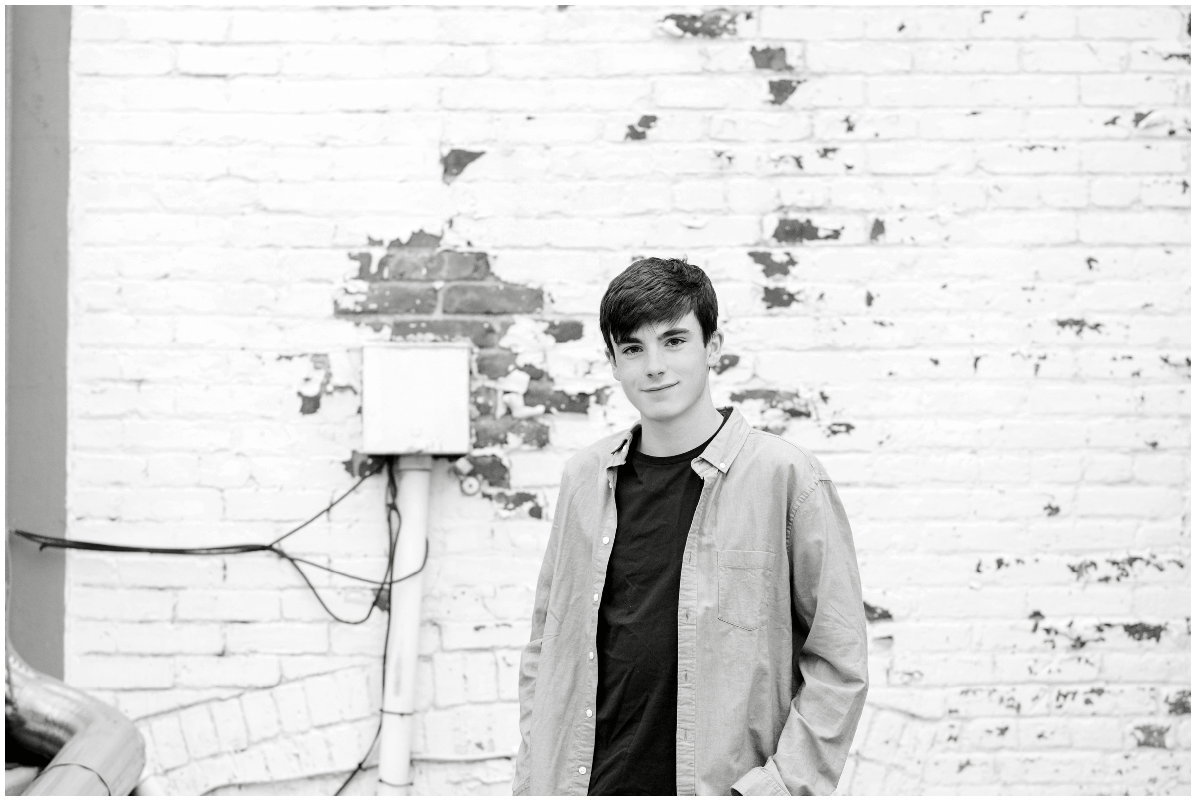 teen guy leaning against white brick wall during urban senior pictures in Longmont Colorado 