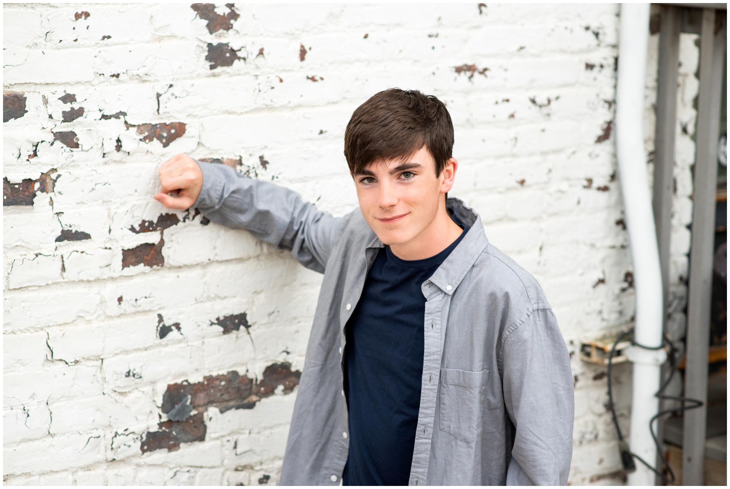 teen guy leaning against white brick wall during urban downtown Longmont Colorado senior portrait session