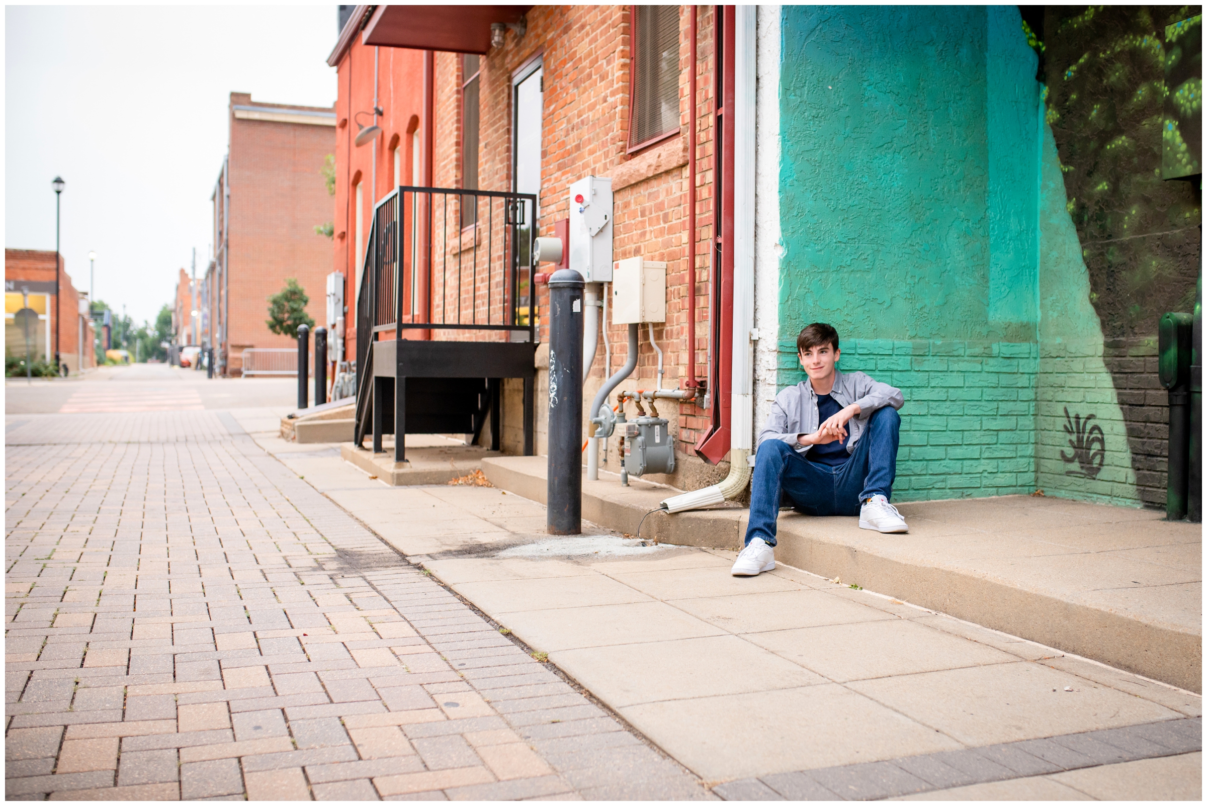 teen guy leaning against bright teal wall during urban senior pictures in Longmont Colorado 