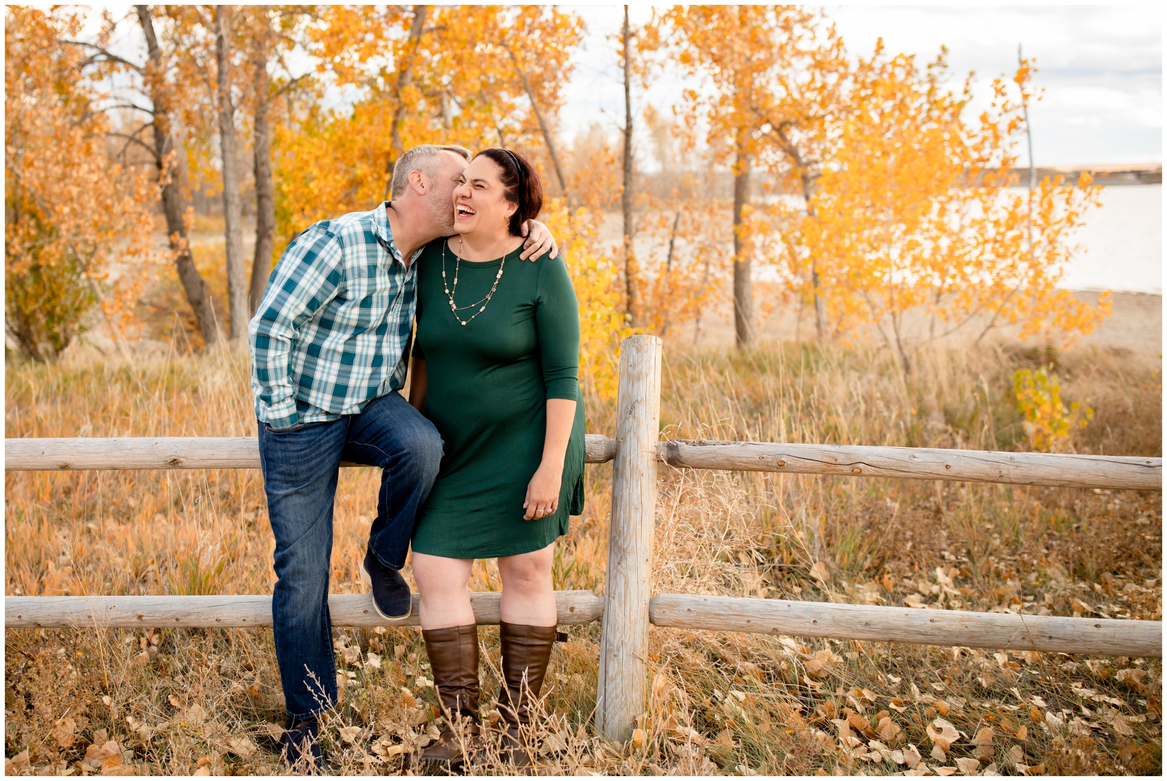 couple leaning against wooden fence in front of colorful fall foliage during  fall engagement pictures in Boulder Colorado 