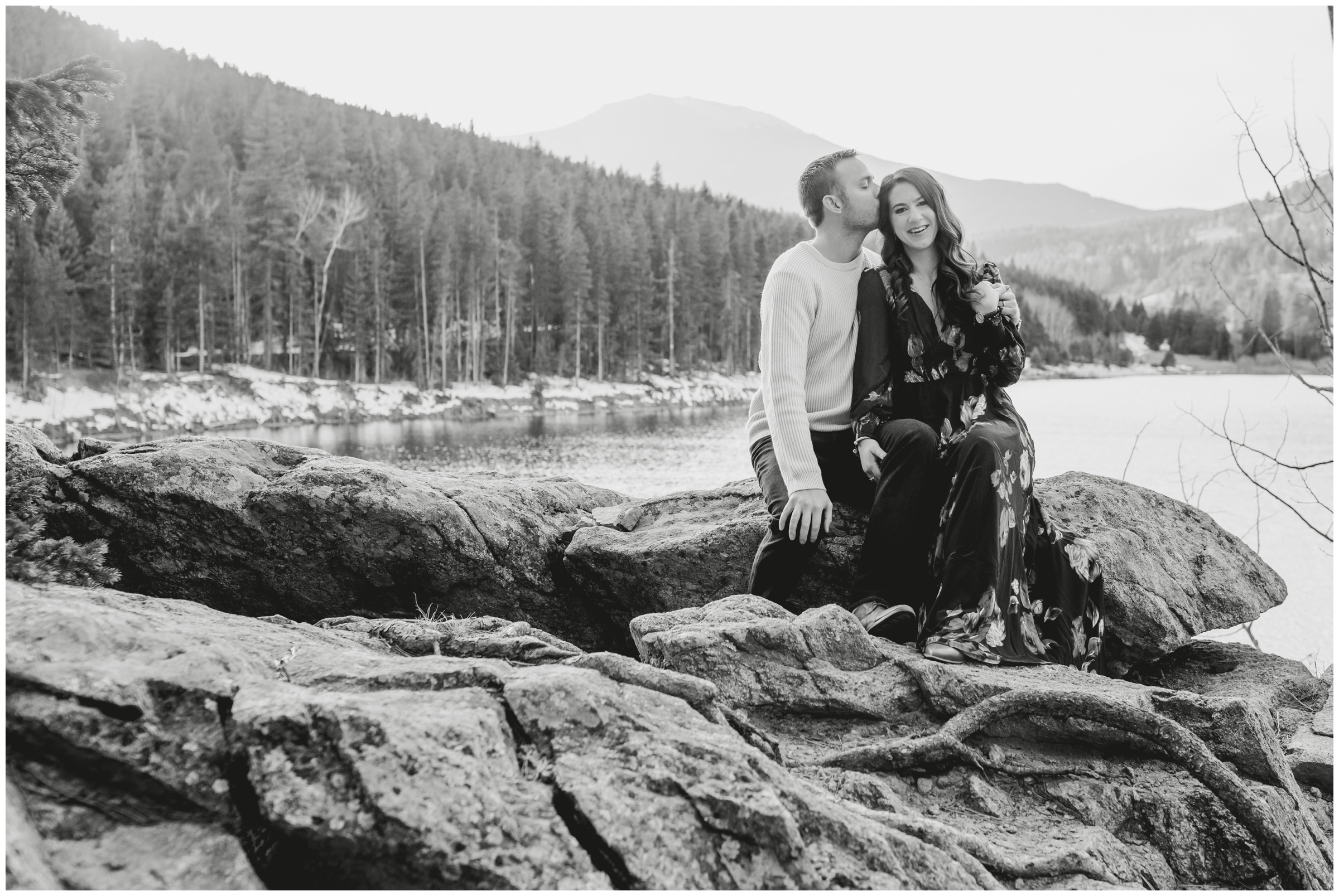 couple cuddling on rock formations with mountains in background during Colorado anniversary photo session in Evergreen 