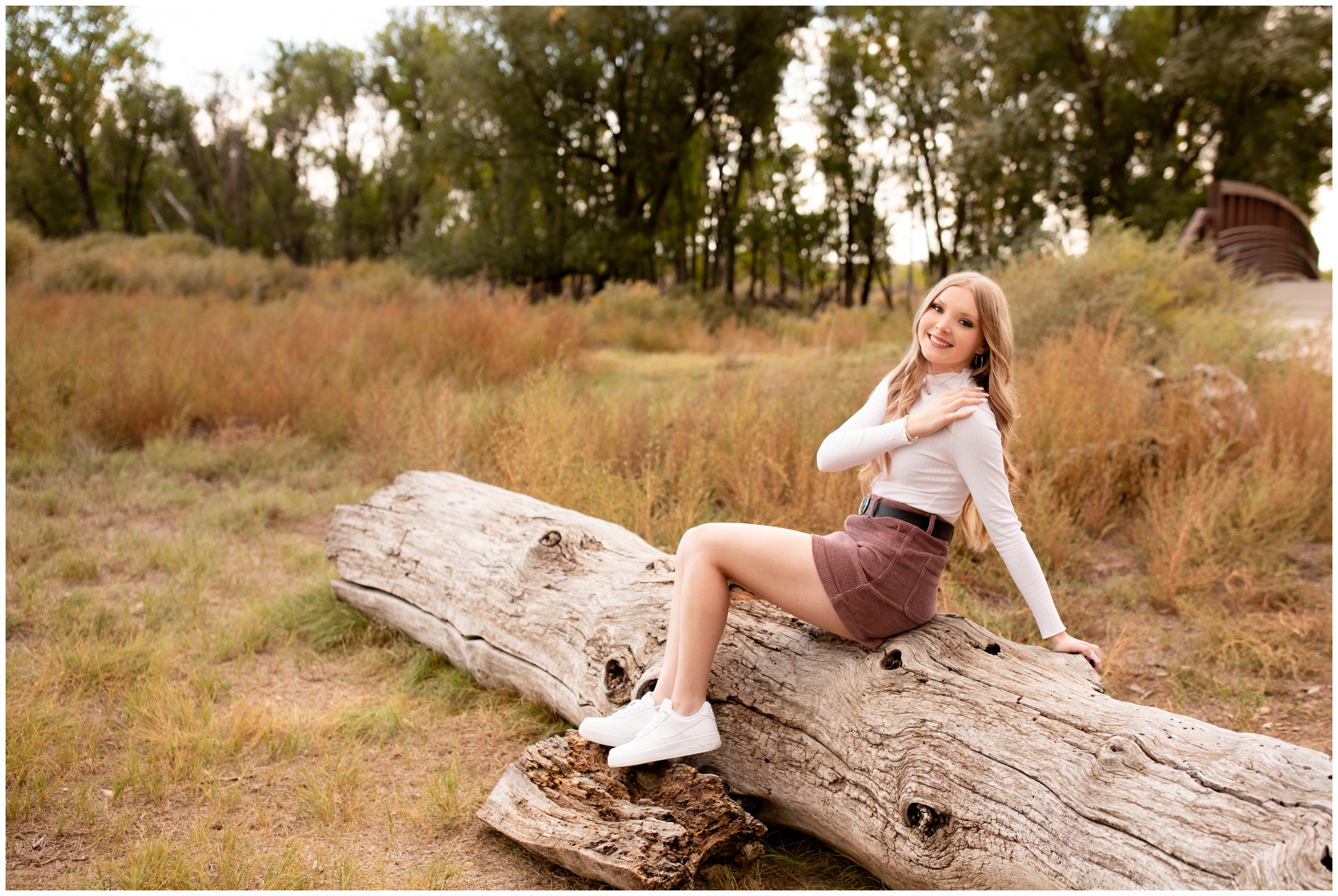 teen girl sitting on downed tree during senior portraits at Sandstone Ranch in Longmont Colorado 