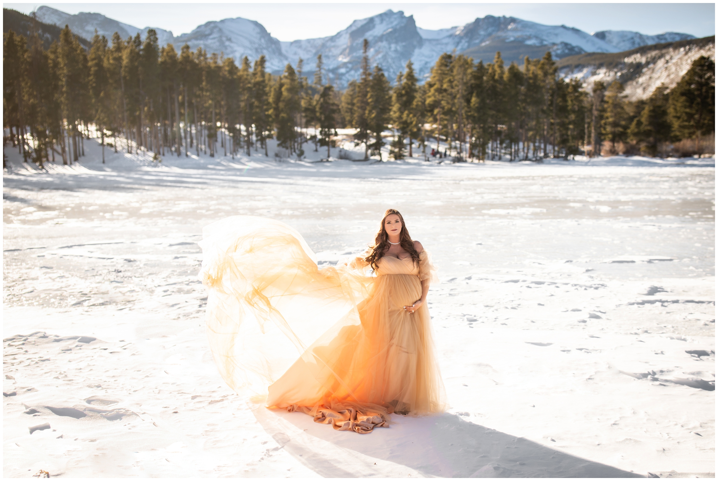 woman posing on frozen lake in Colorado mountains during winter maternity photography session 