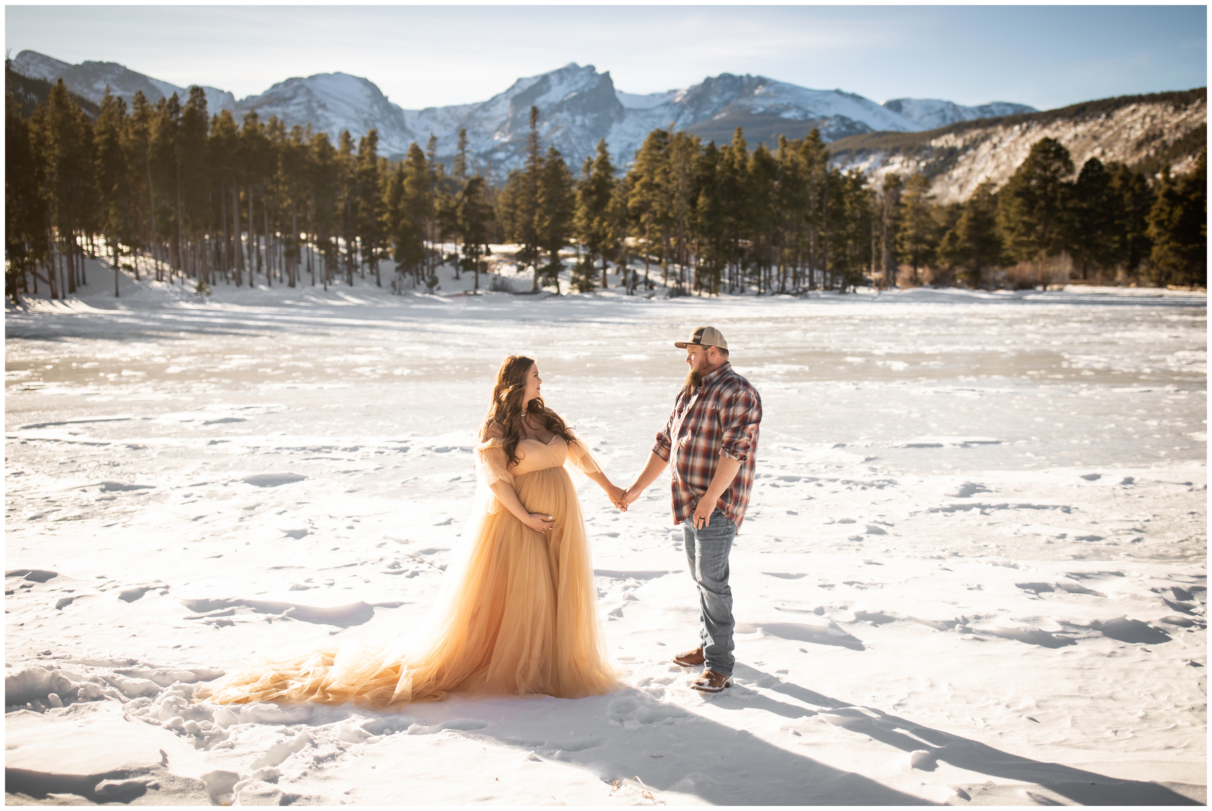 couple holding hands on a frozen lake during winter maternity portraits in Estes Park Colorado 