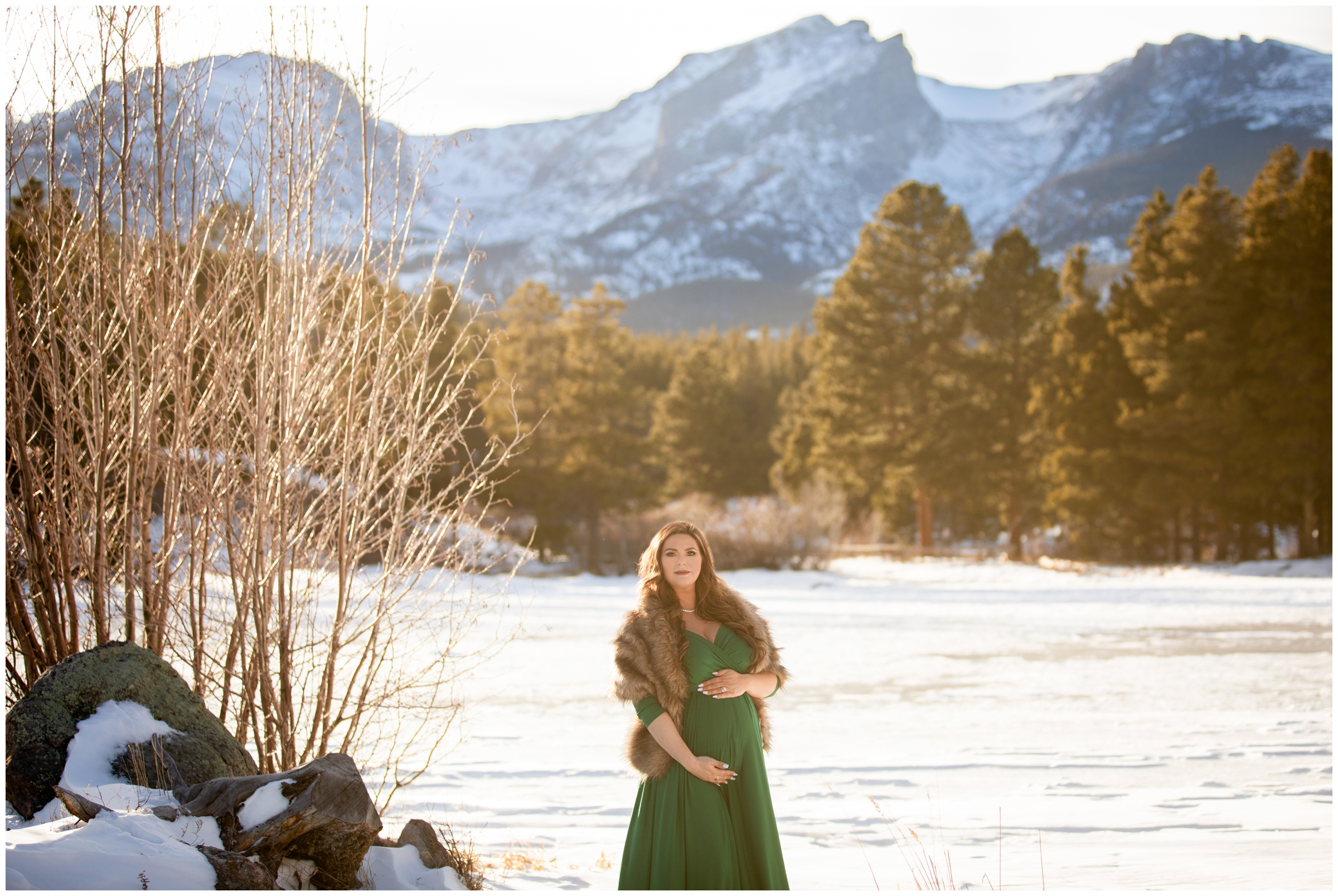 woman standing on frozen lake in kelly green maternity gown during winter pregnancy pictures in Estes Park Colorado 