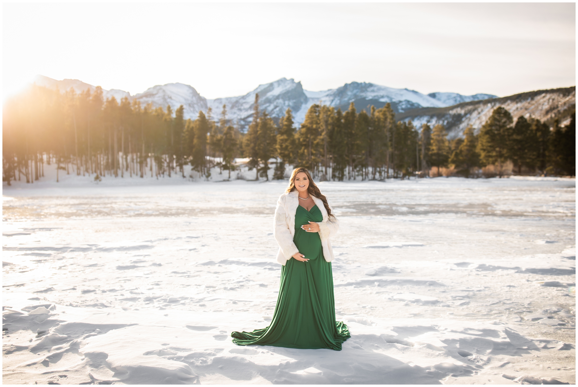 woman in green dress standing on frozen lake during winter maternity photography session in Estes Park Colorado