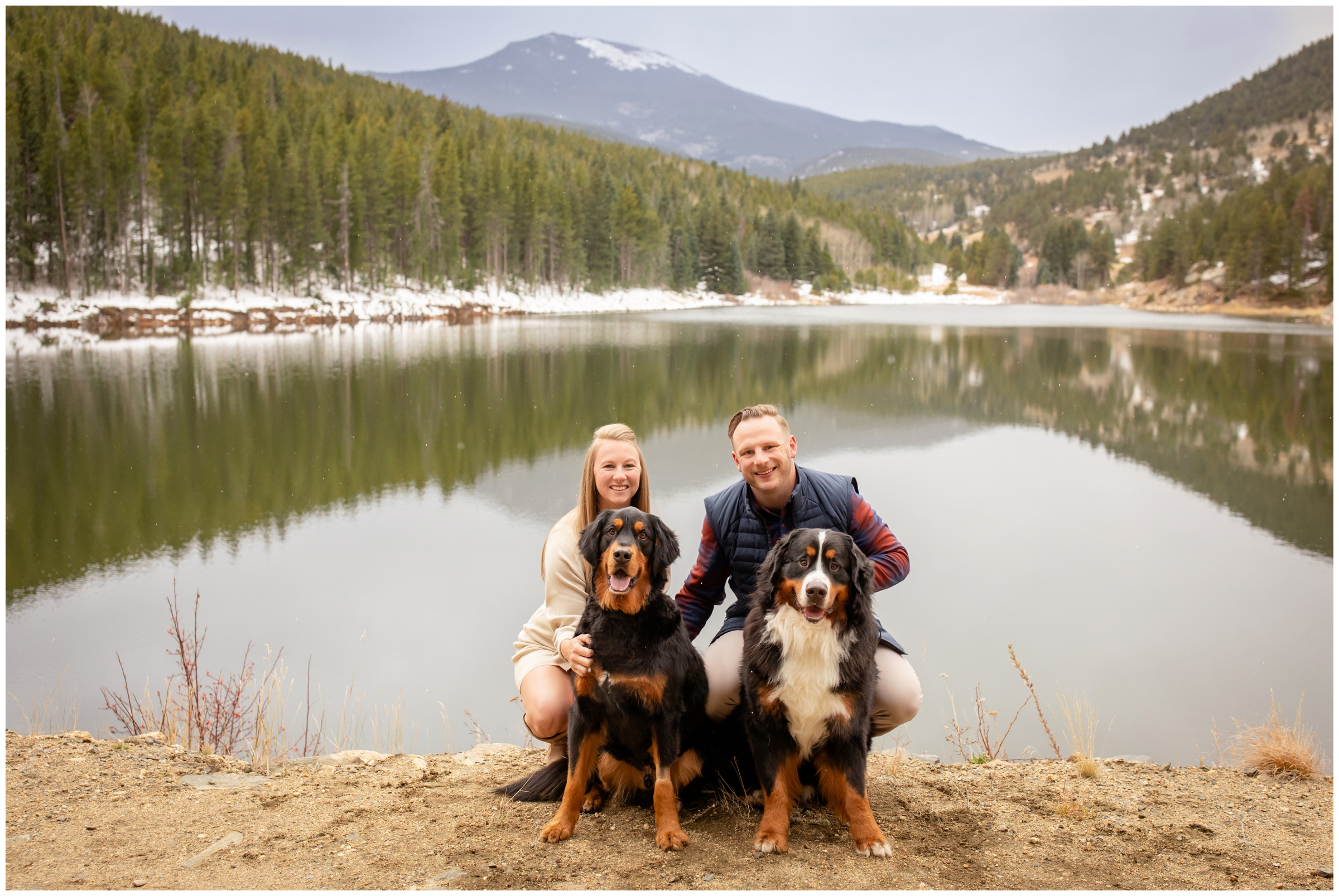couple posing with their dogs with mountain lake in the background during evergreen Colorado anniversary photo shoot