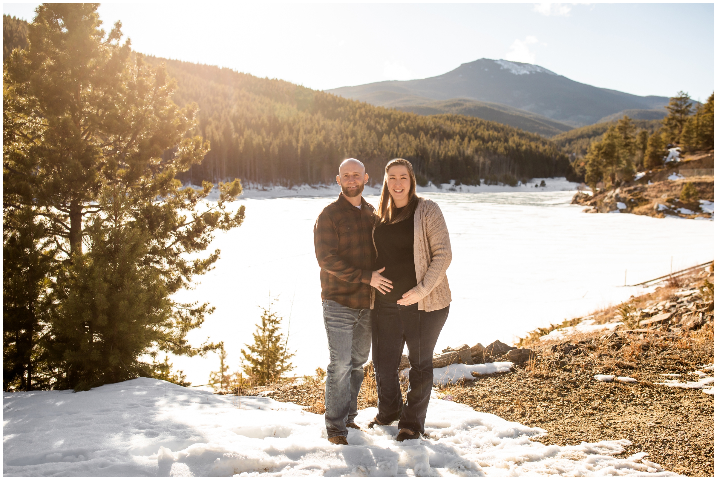 couple posing in front of frozen mountain lake during Colorado winter maternity session 