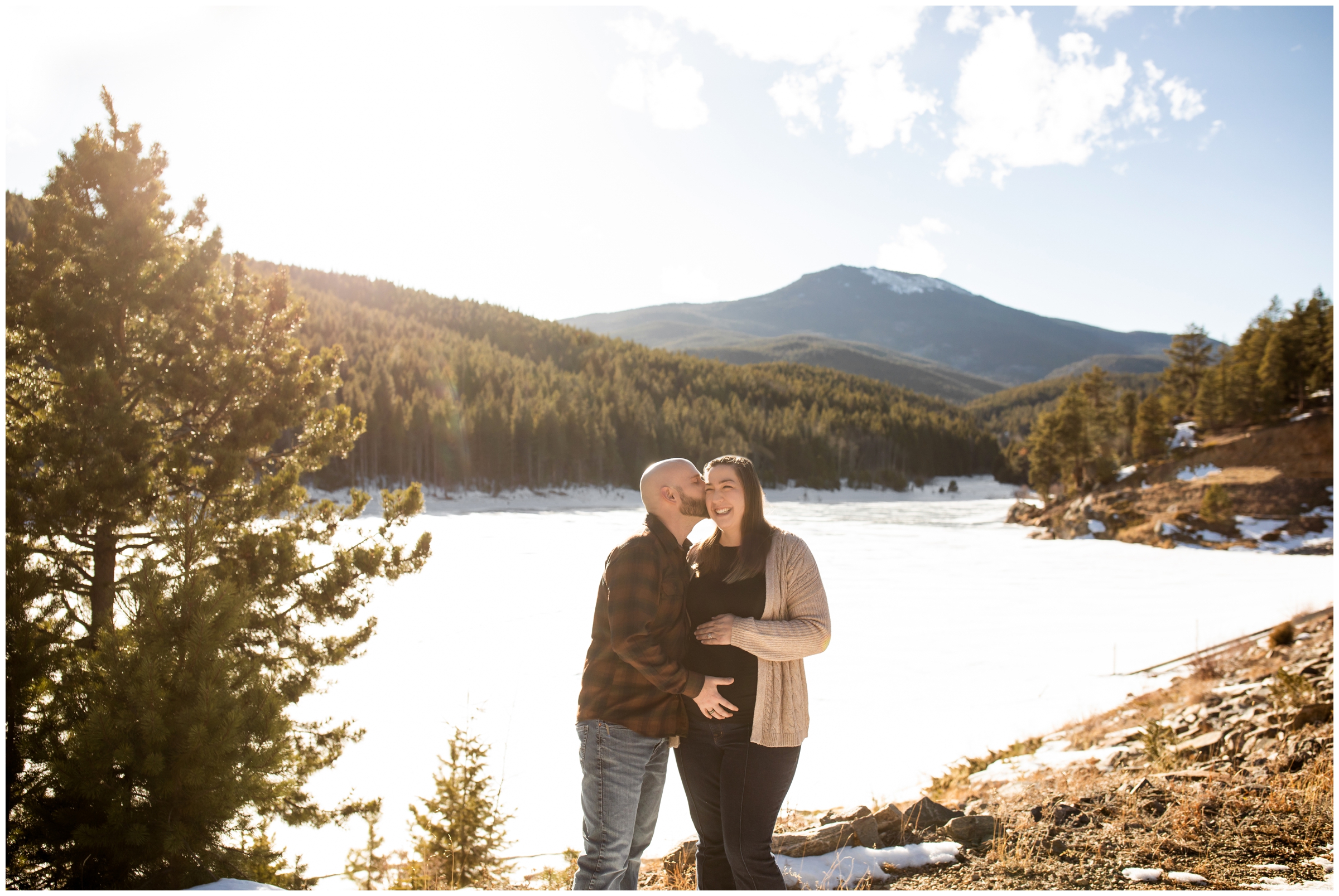 couple posing in front of frozen mountain lake during Evergreen Colorado winter maternity portraits
