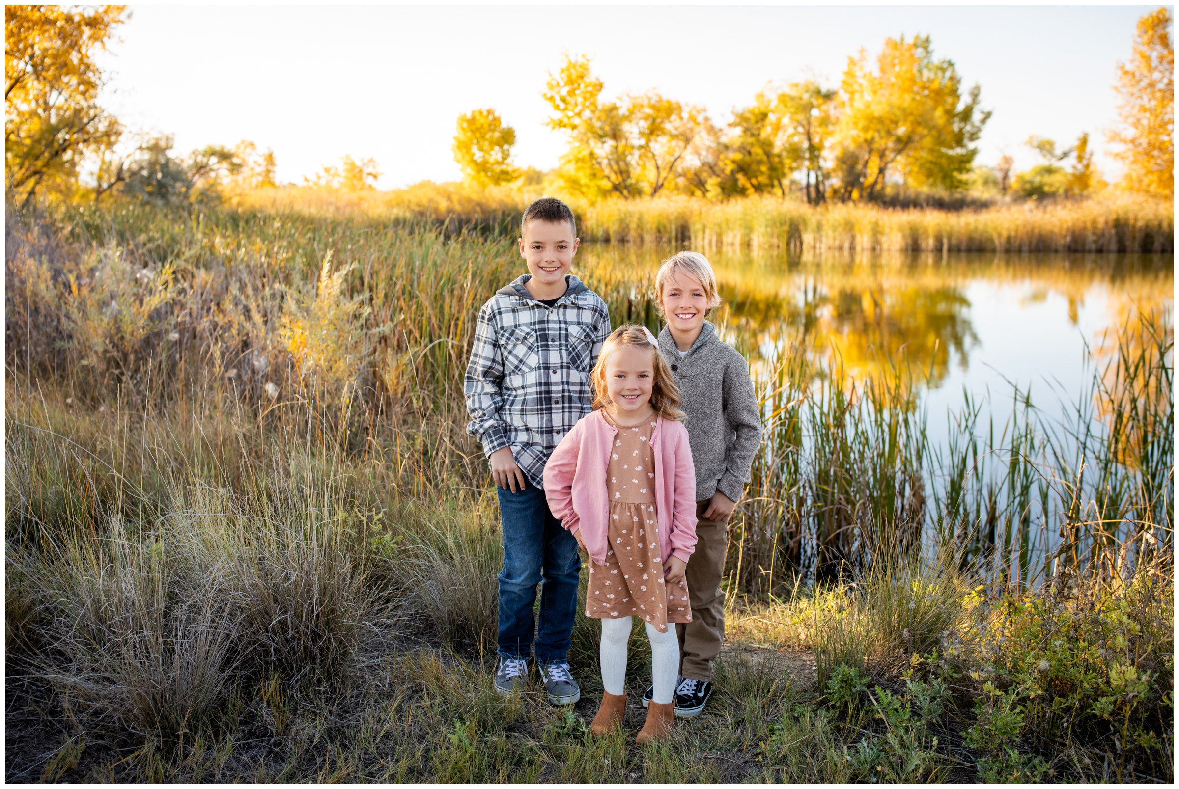 kids posing in front of lake with colorful fall foliage during Longmont Colorado family portraits 