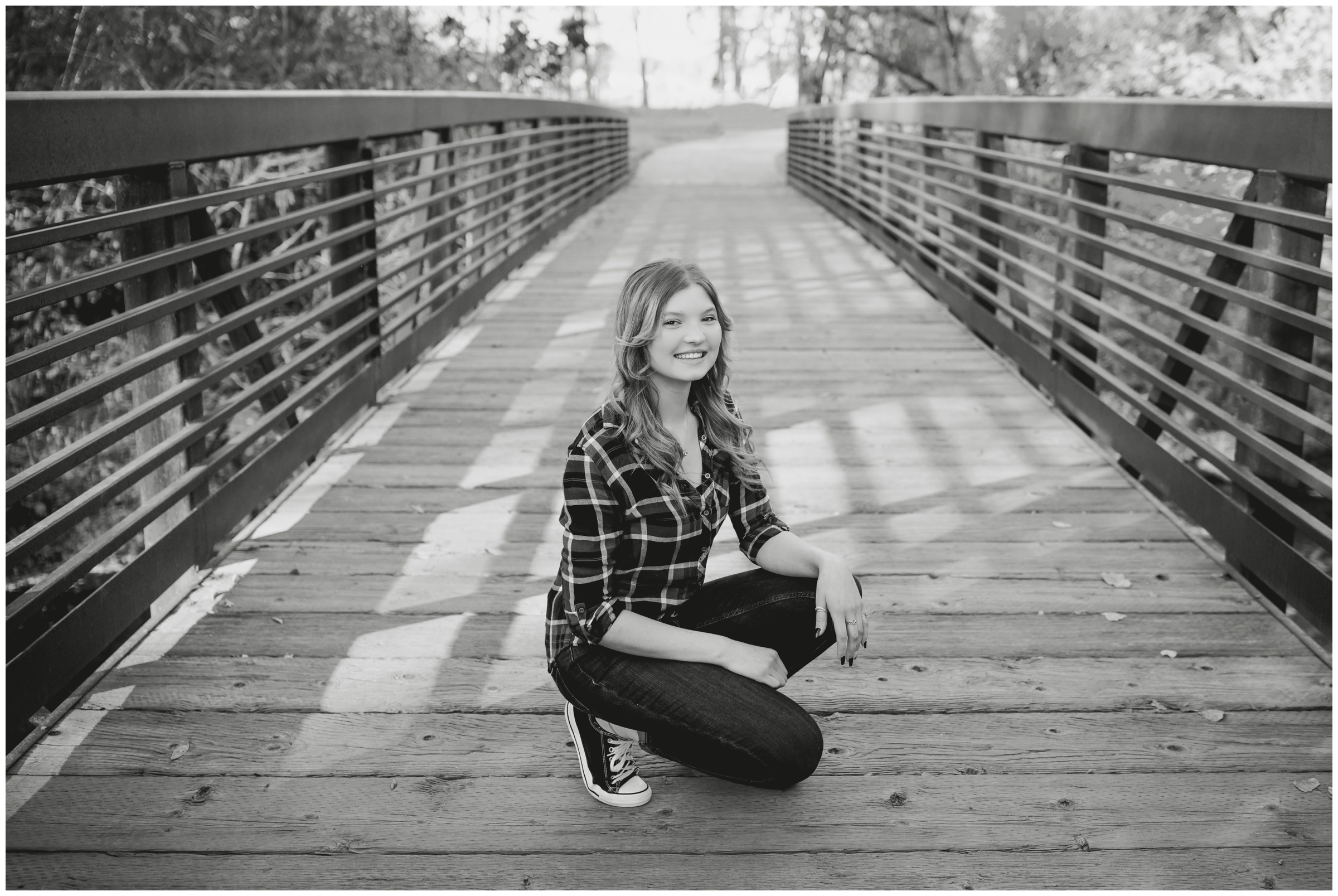 teen girl squatting on bridge during senior photography session at Golden Ponds in Longmont Colorado 