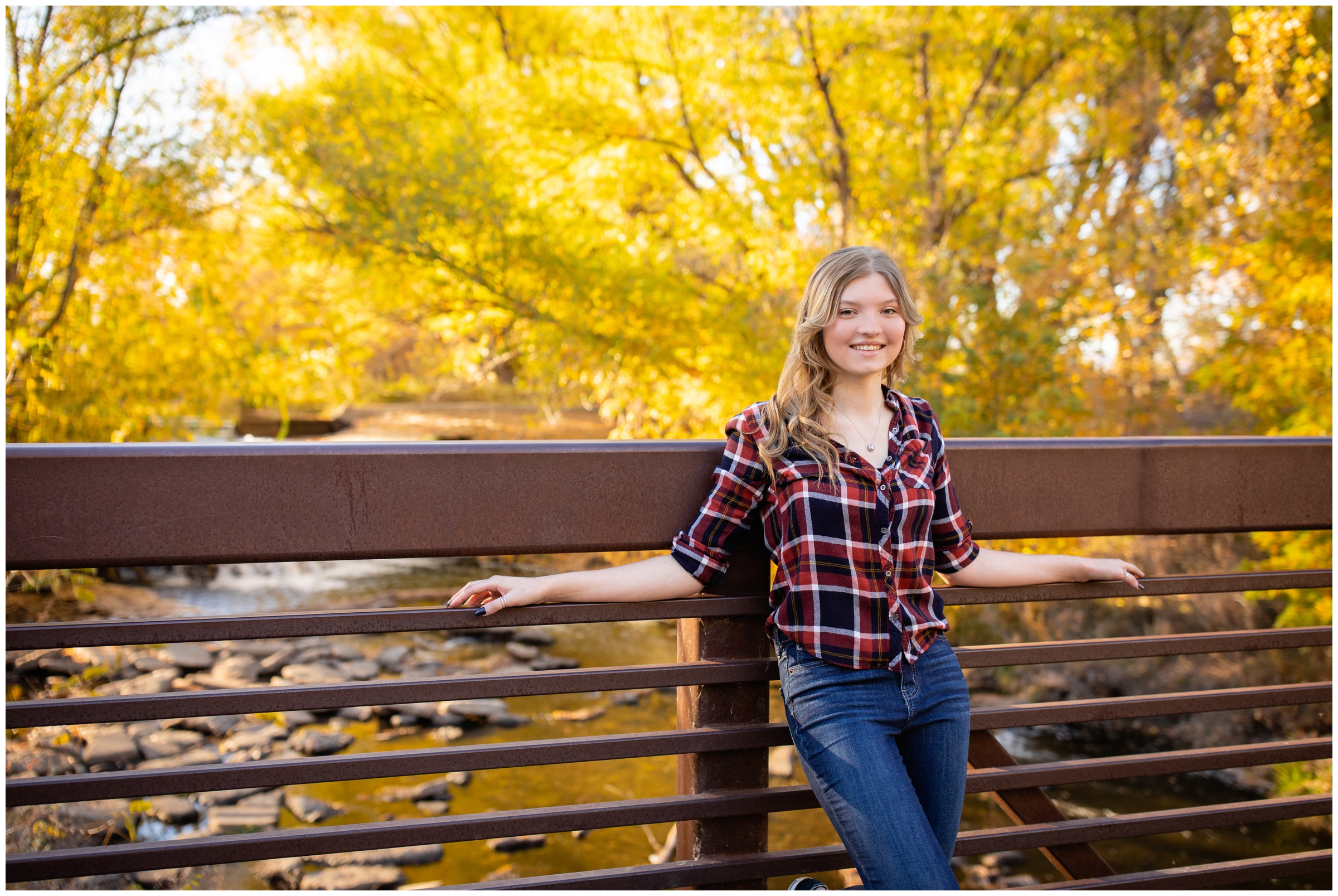 teen posing on bridge with colorful fall foliage in the background during Longmont fall senior photos at Golden Ponds