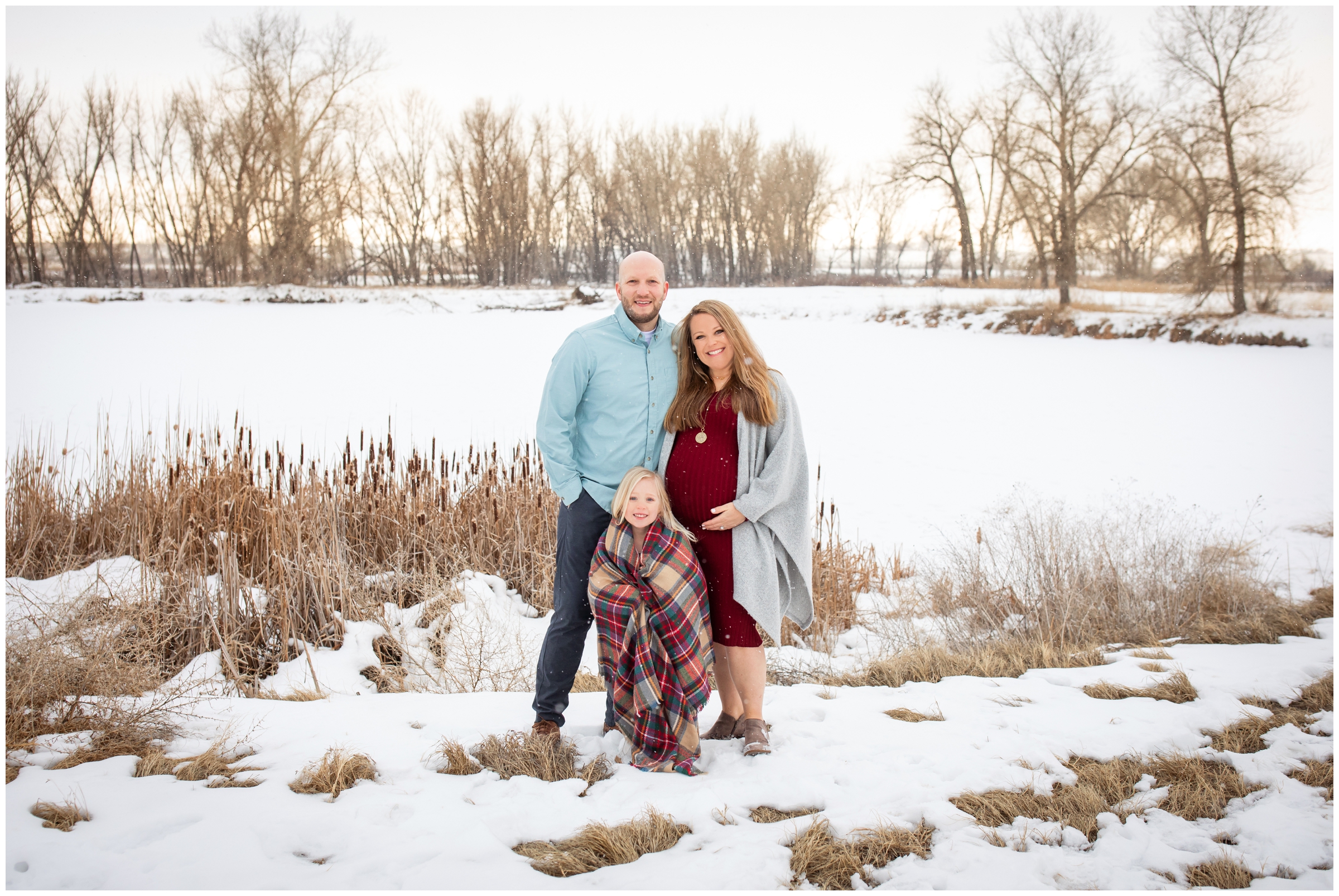 family of three posing in front of snowy lake at sandstone ranch during Longmont winter family photos