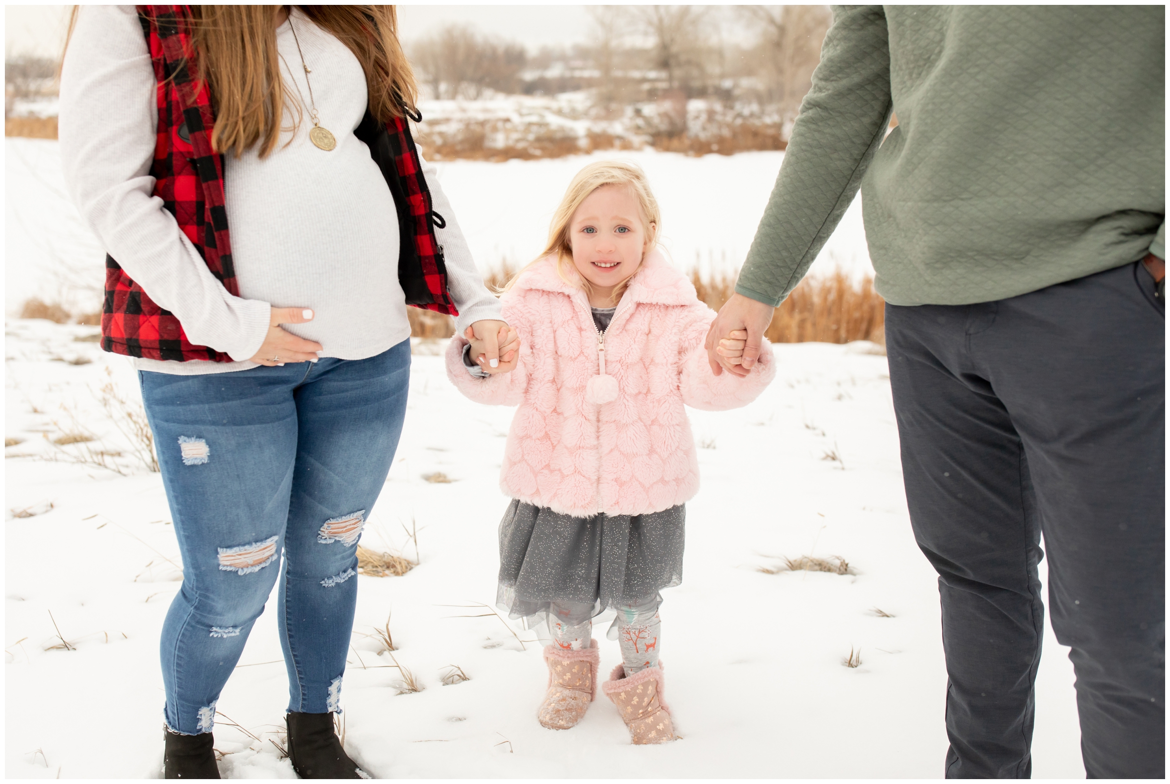 little girl holding parents hands during snowy winter family photography session in Longmont Colorado