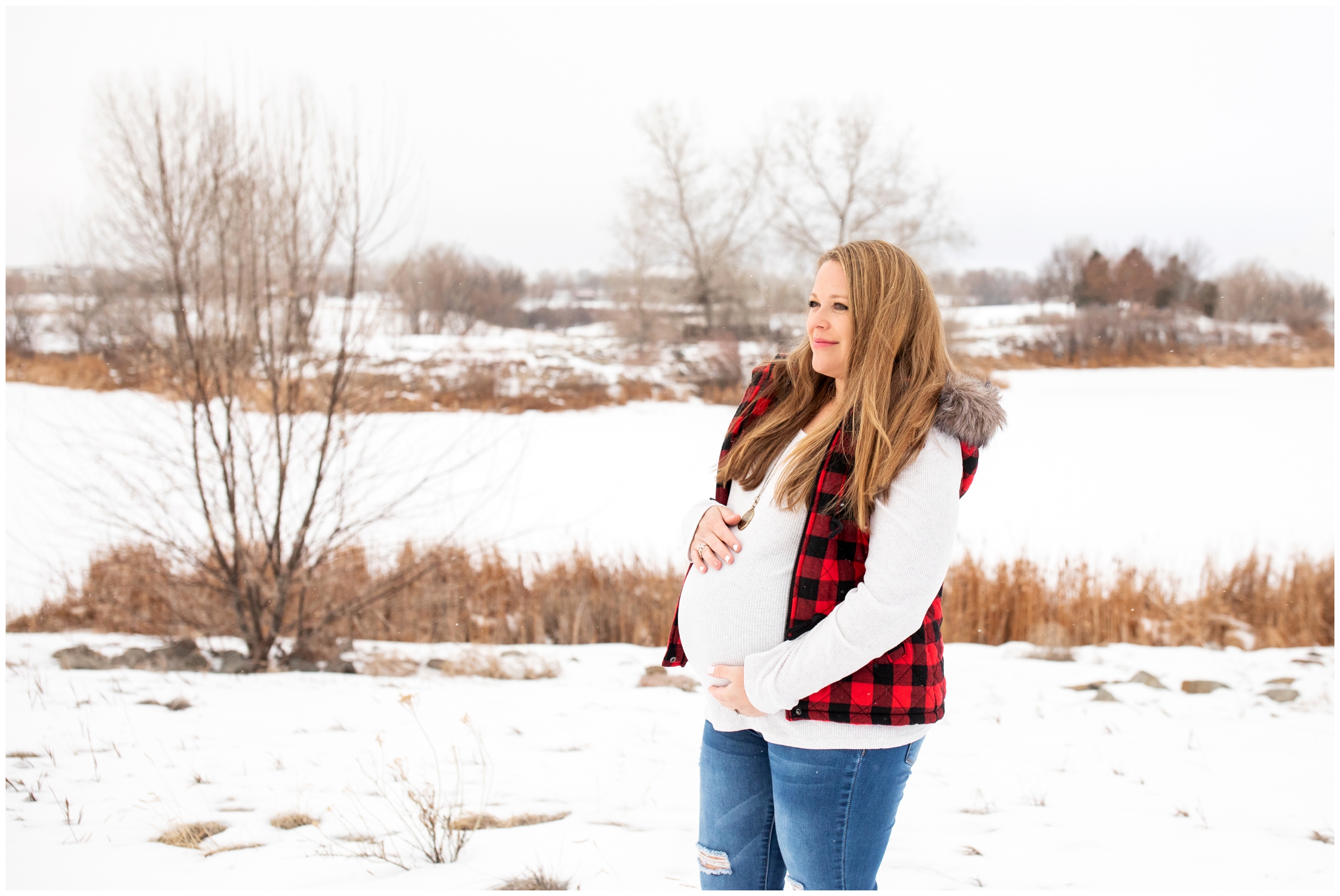 woman in buffalo check vest posing in the snow for winter maternity portraits at Sandstone ranch in Longmont 