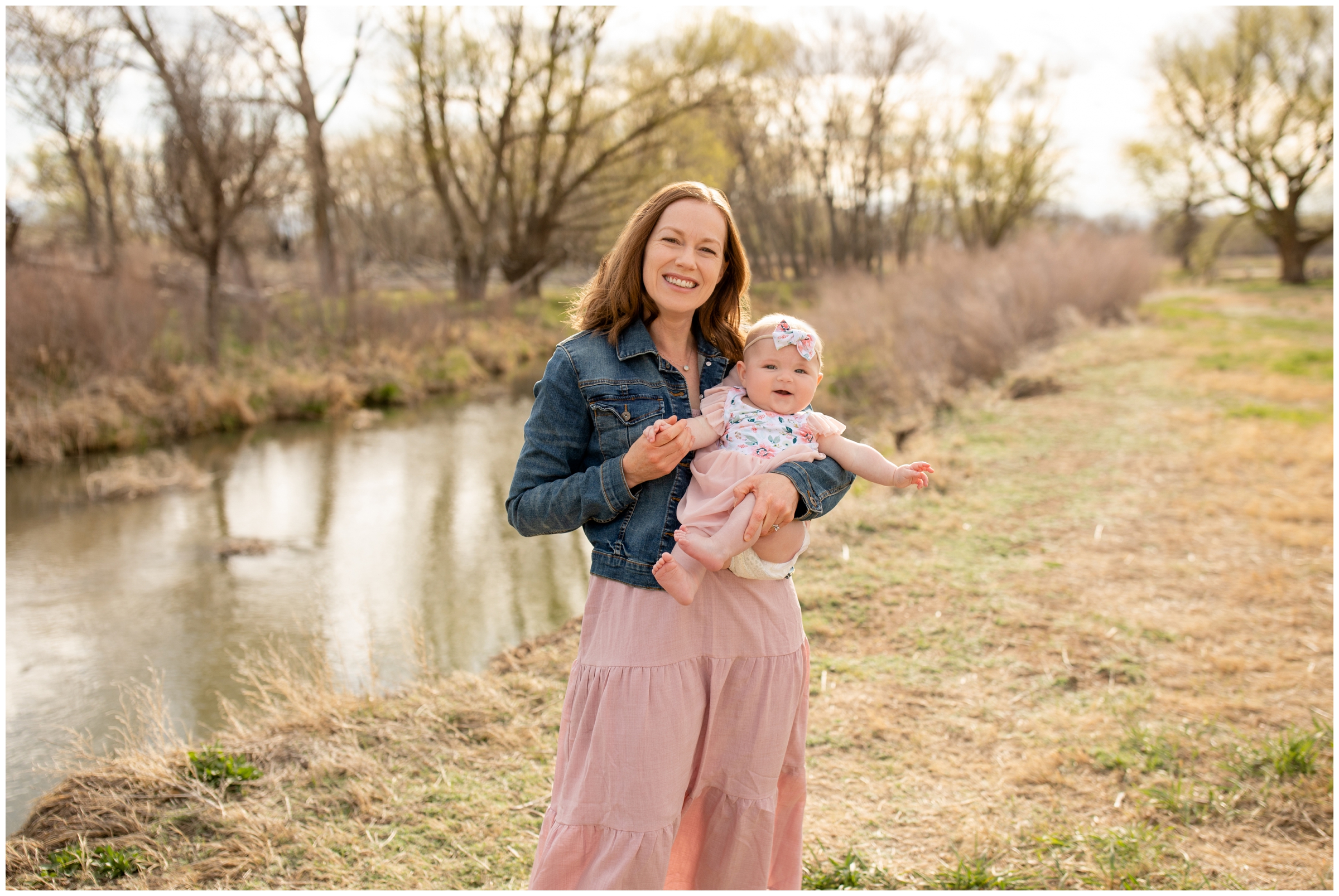mom holding baby daughter next to river during Longmont family portraits at Sandstone Ranch