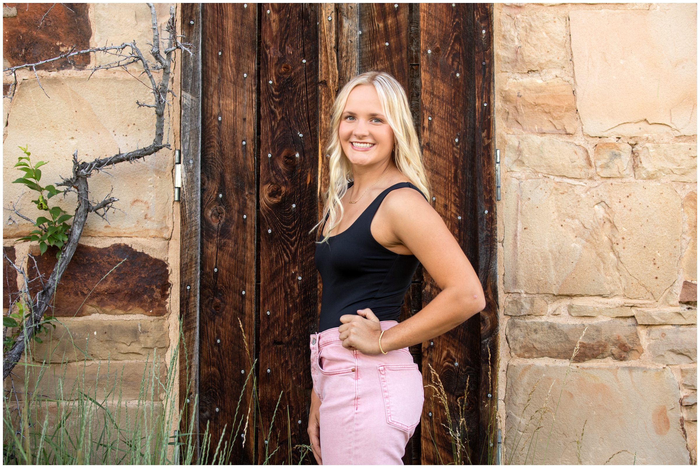 teen posing in front of stone and wood wall during senior portraits at south Mesa Trail in Colorado 