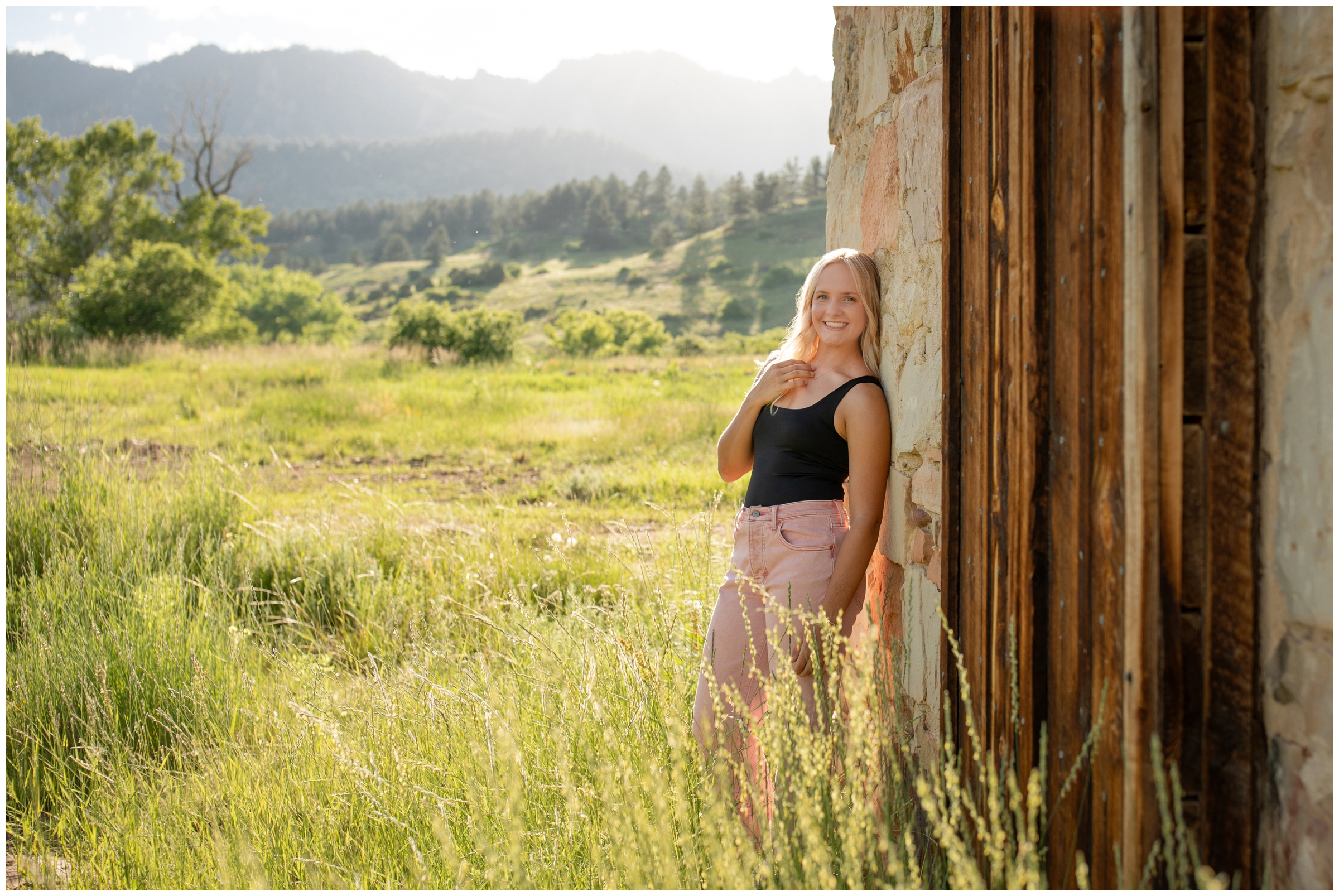 teen leaning against wooden and stone wall with mountains in background during Boulder graduation pictures at South Mesa Trail by Colorado senior portrait photographer Plum Pretty Photography