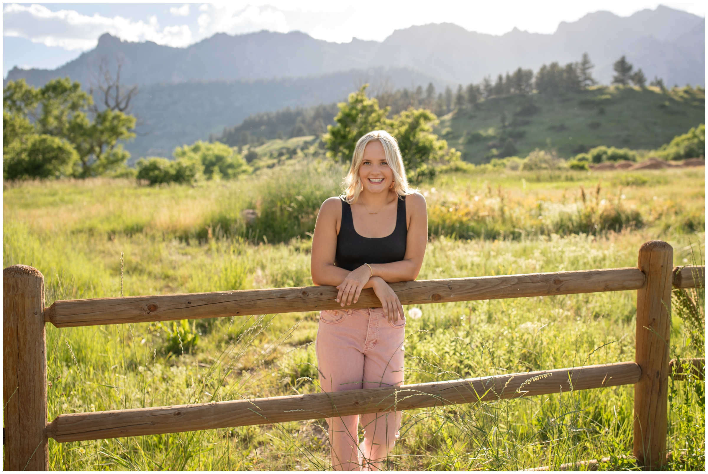 teen leaning on fence with mountains in background during Boulder graduation senior portraits at South Mesa Trail