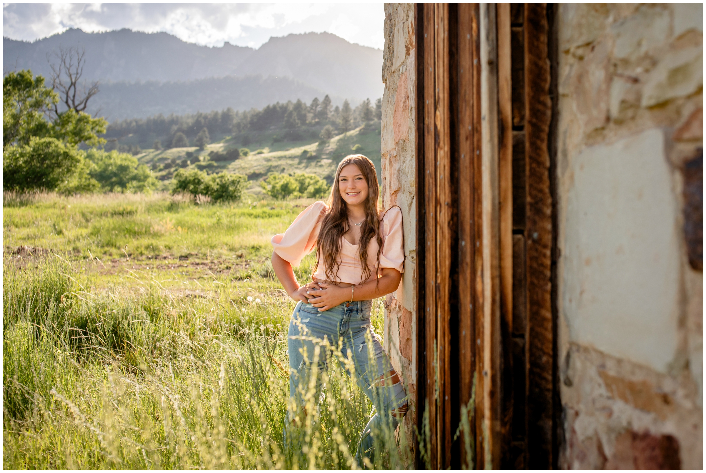 teen leaning against wood wall with mountain backdrop during Boulder senior portrait images at South mesa trail