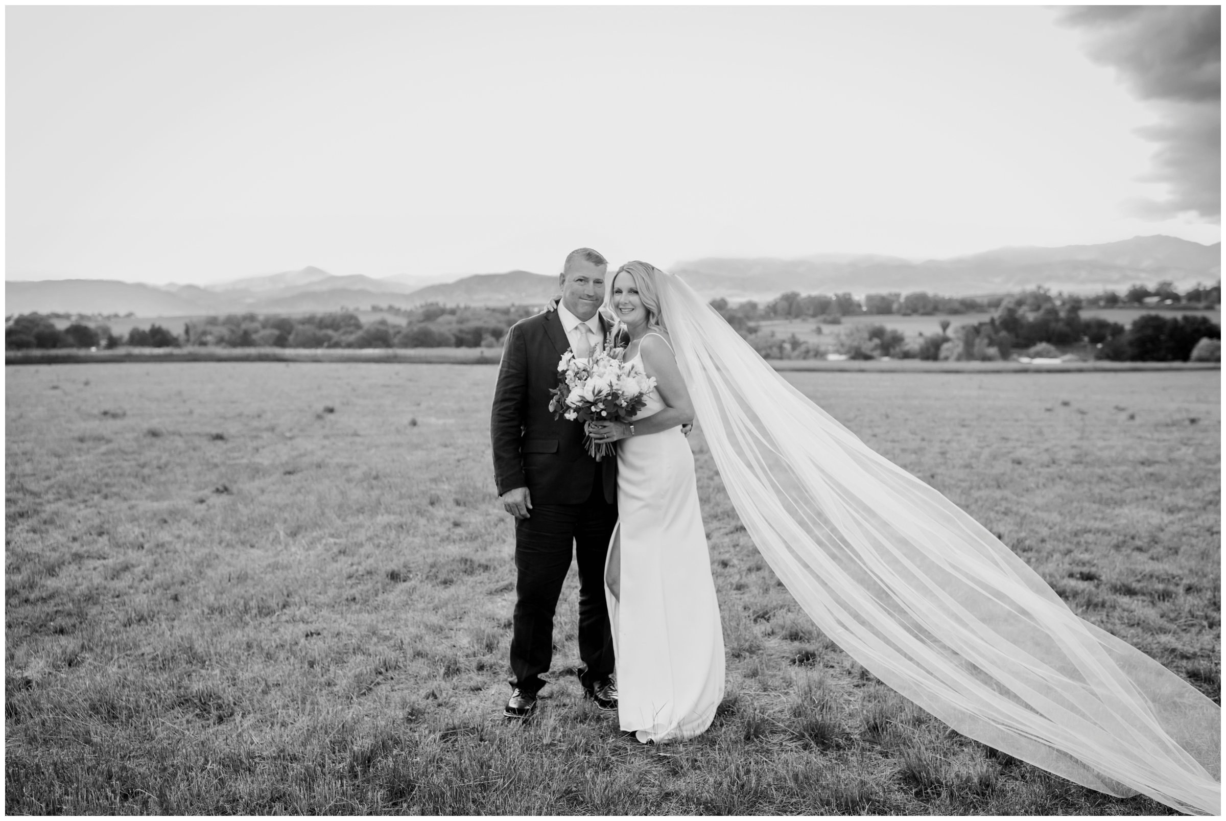 black and white photo of bride and groom posing in a field with flatirons in the background during Boulder Colorado wedding photos