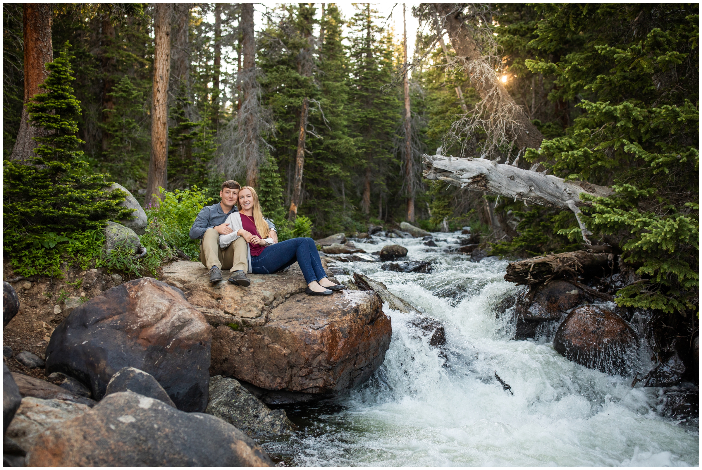 couple sitting on large rock next to mountain river in Colorado mountains during engagement portraits 