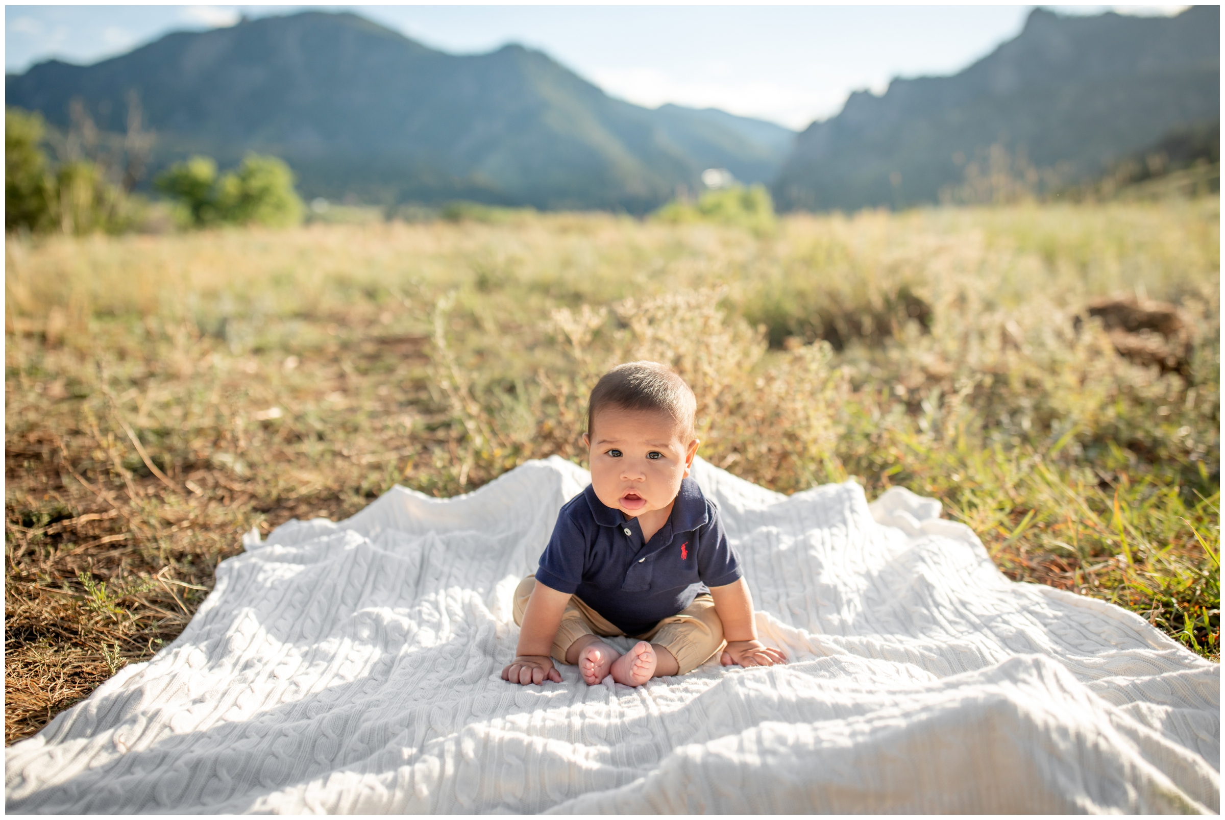 baby sitting on blanket with mountains in background during family portraits at South Mesa Trail in Boulder Colorado 