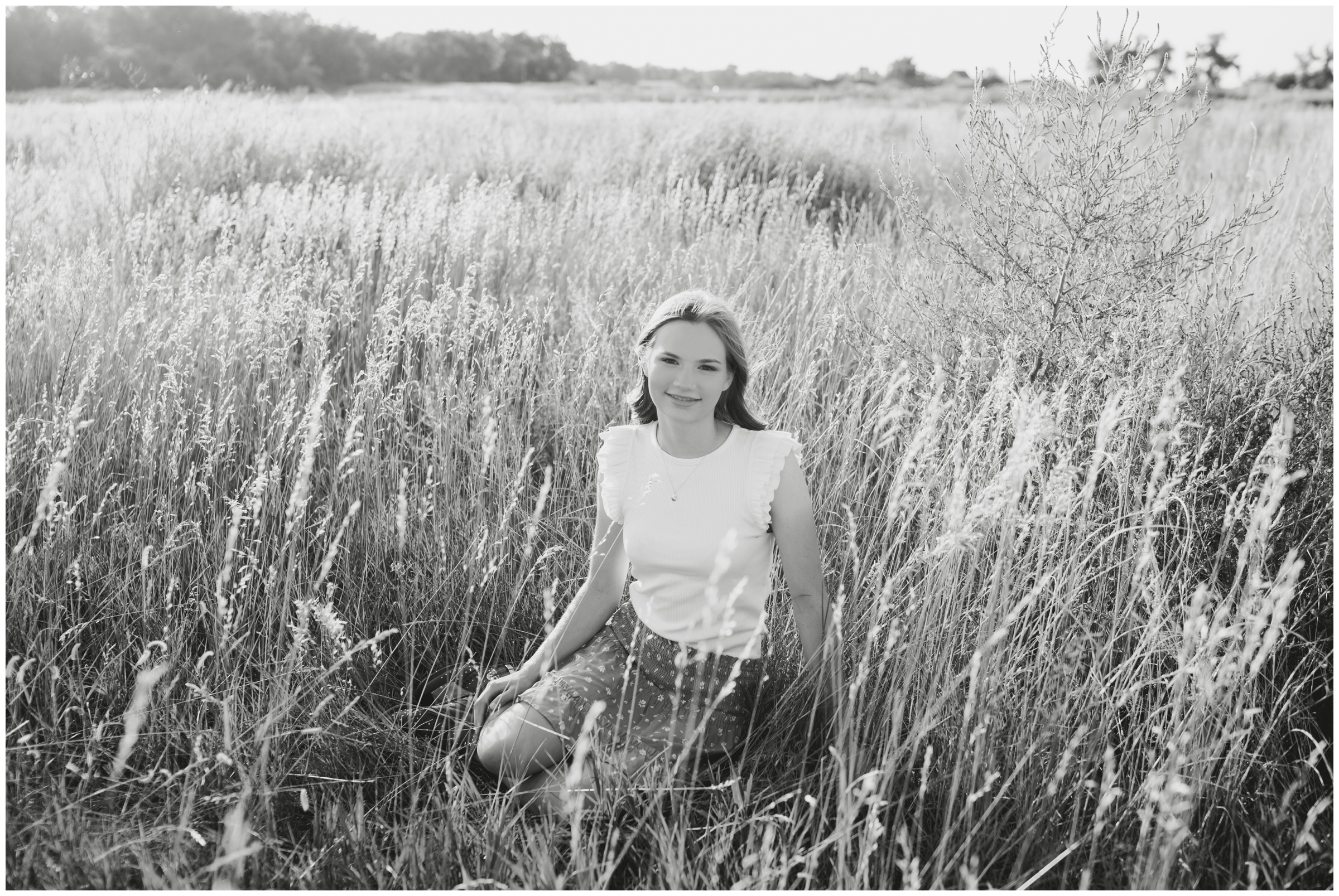 teen sitting in field of long grasses during rustic Colorado senior portraits at 17 mile house farm park 