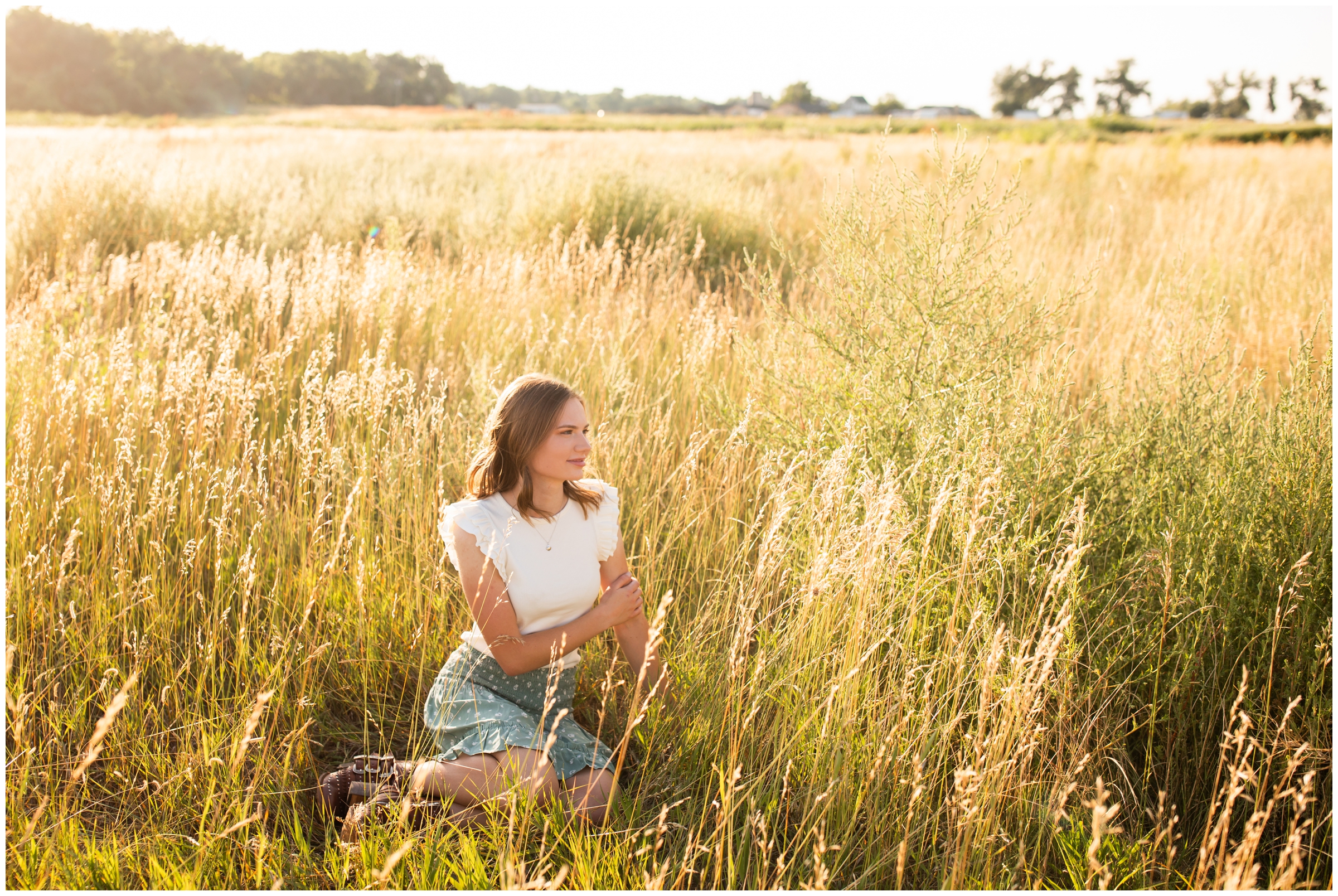 teen sitting in golden field of long grasses during Centennial Colorado senior photos