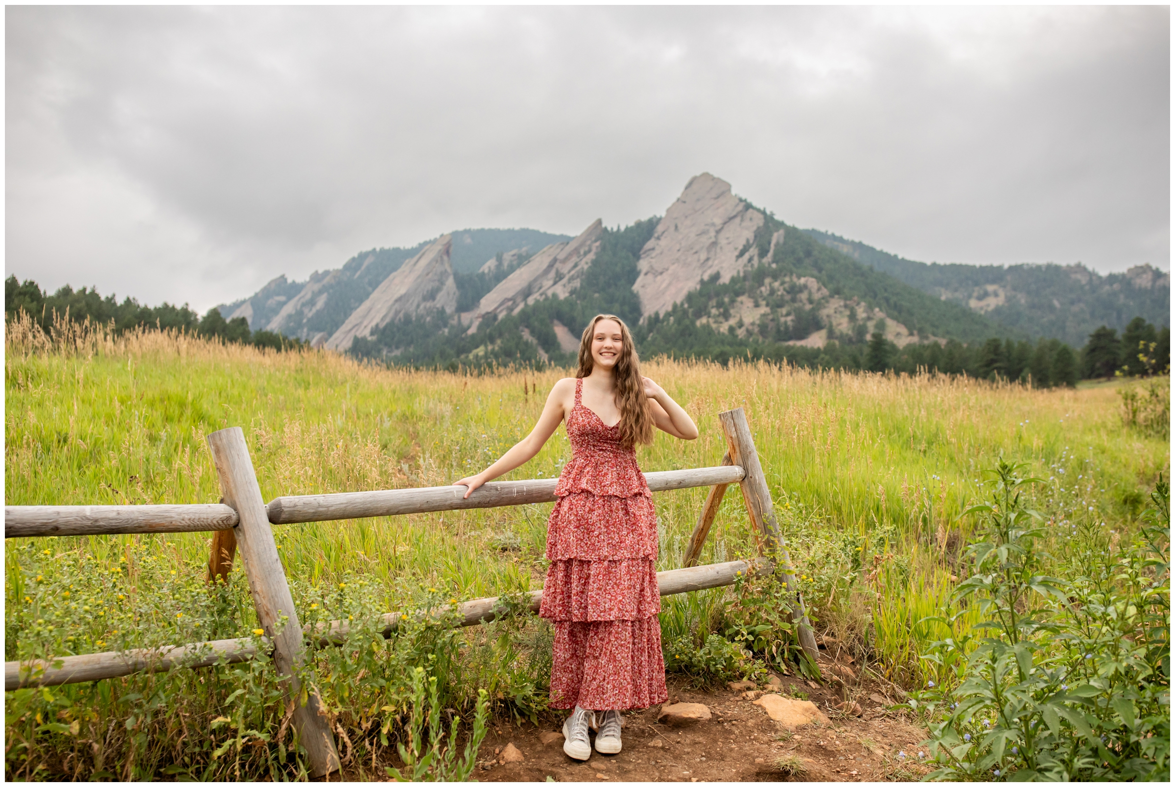 teen leaning on fence with mountains in background during Chautauqua senior photos in Boulder Colorado 