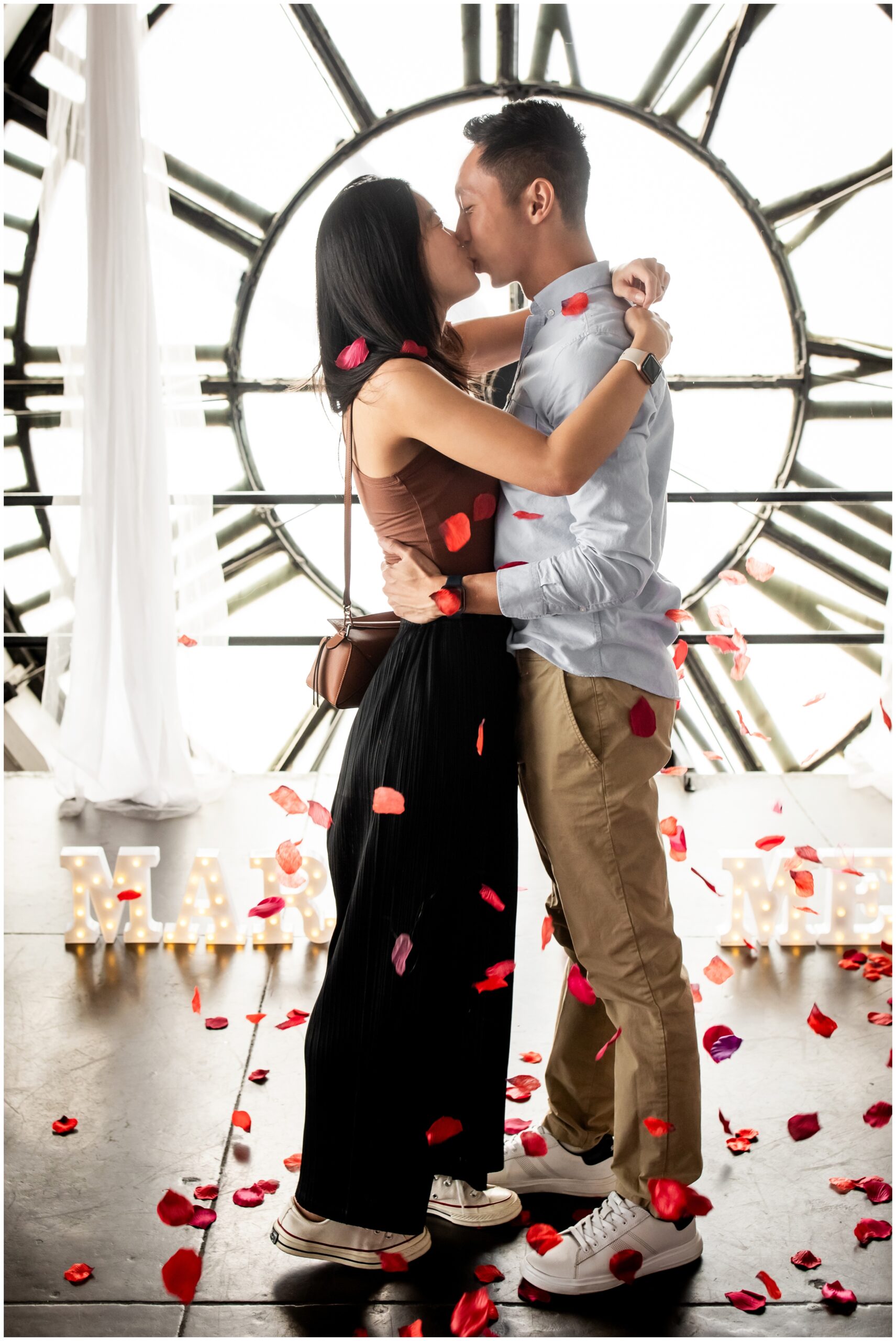 couple kissing as rose petals fall around them during Denver proposal photos at the Clock tower events 
