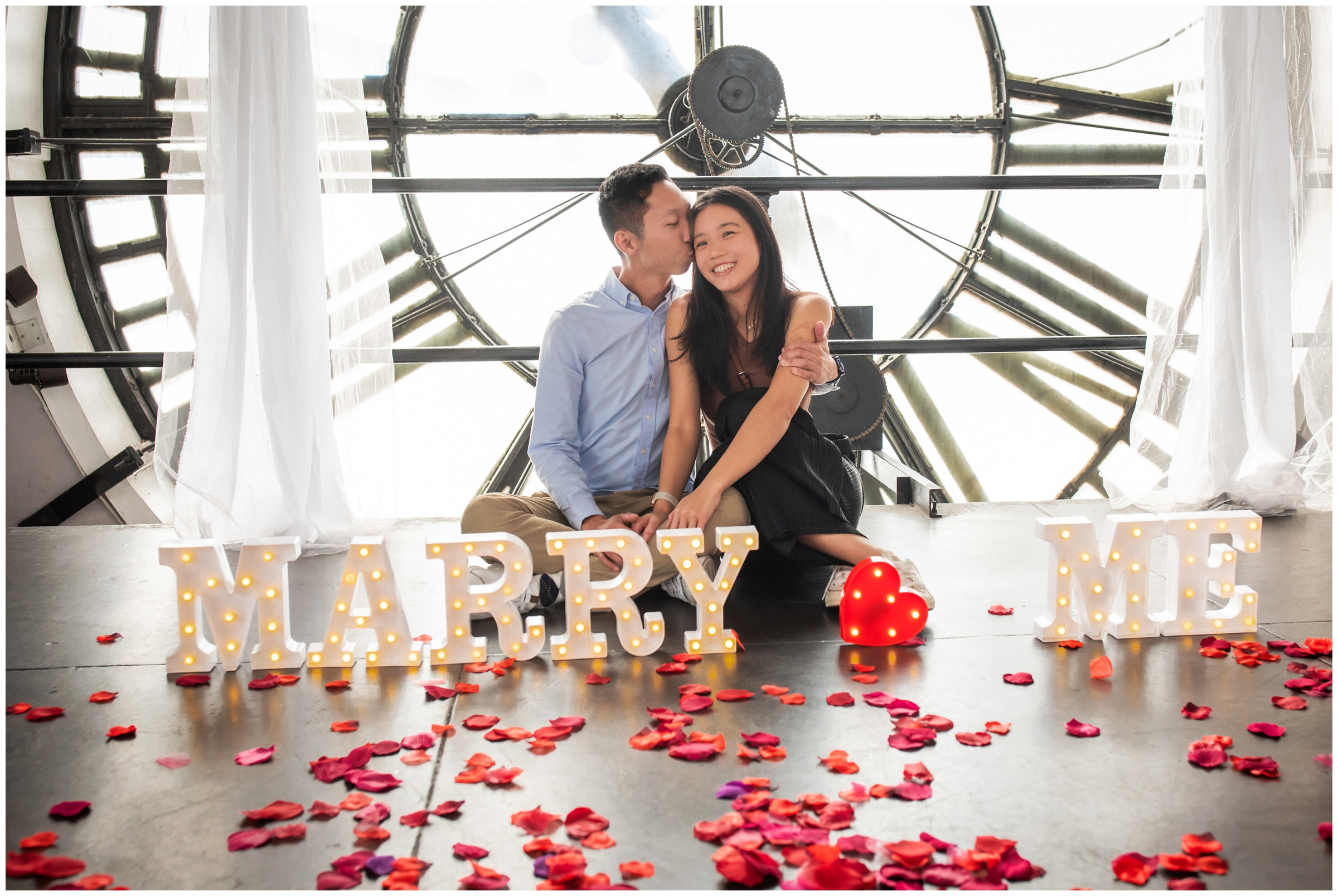 couple cuddling in front of the clocktower during Denver proposal engagement session by Plum Pretty Photography