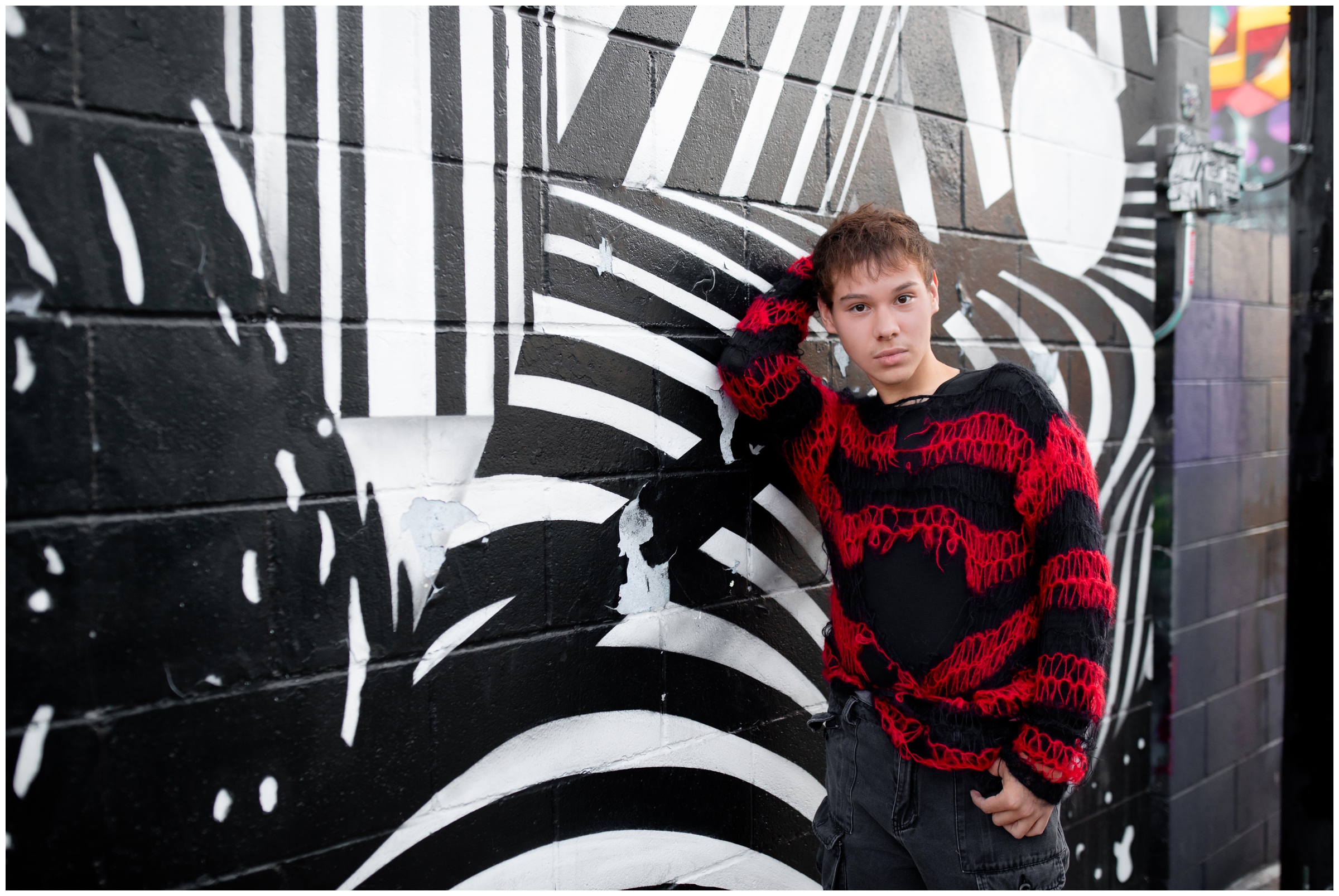teen guy leaning against black and white painted wall during senior portraits in Denver Colorado at the RINO art district