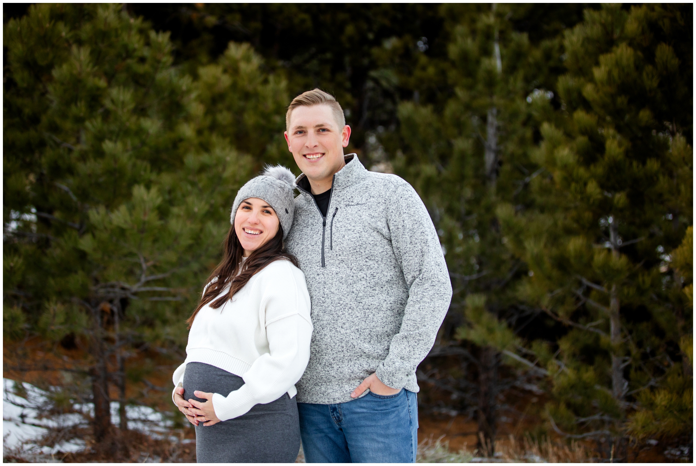 couple posing in front of pine trees during winter maternity pictures in Estes Park Colorado 