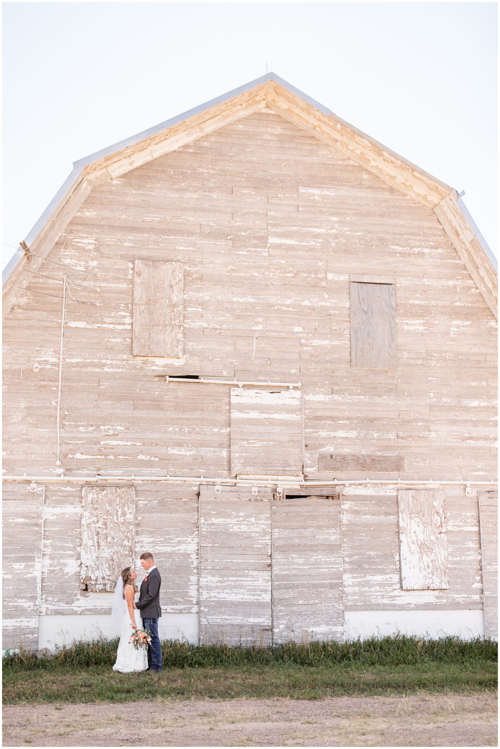 couple posing in front of large rustic barn during Haxtun Colorado farm wedding photos by Plum Pretty Photography 