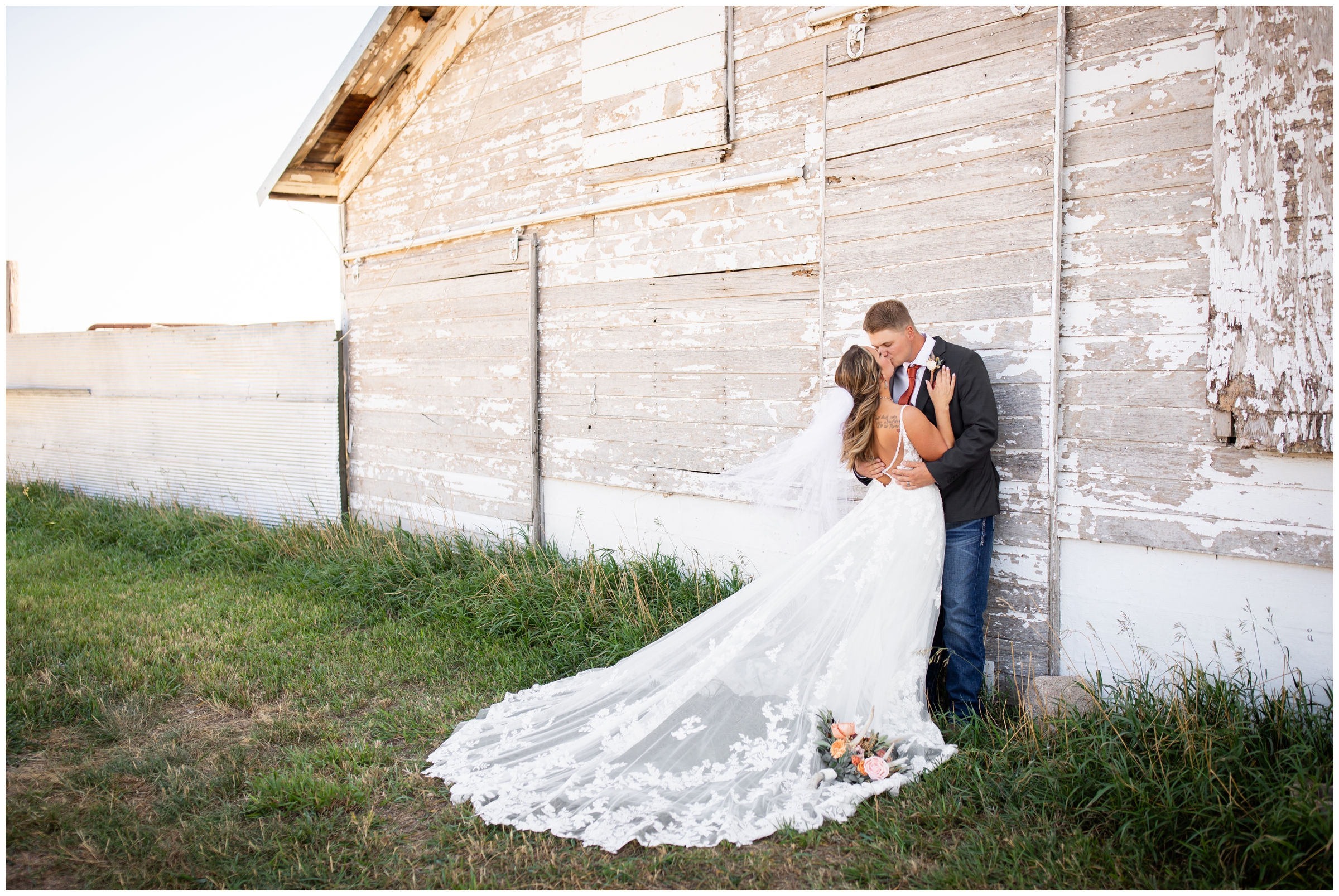 couple leaning against a barn and kissing during romantic wedding pictures in Haxtun Colorado