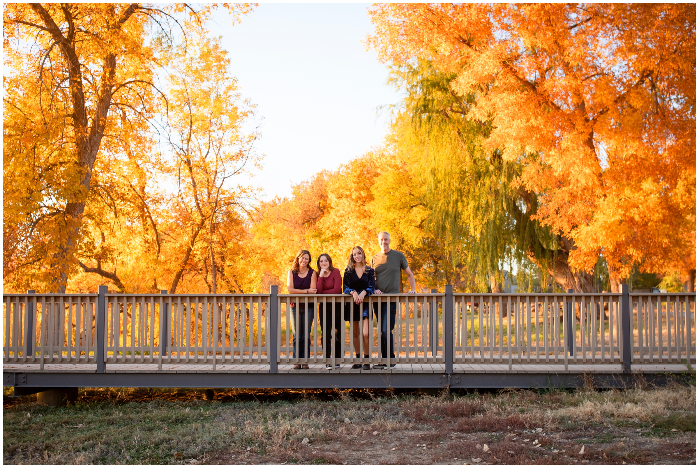 family posing on bridge with colorful fall foliage in background during Mead Colorado family pictures at Highland Lake