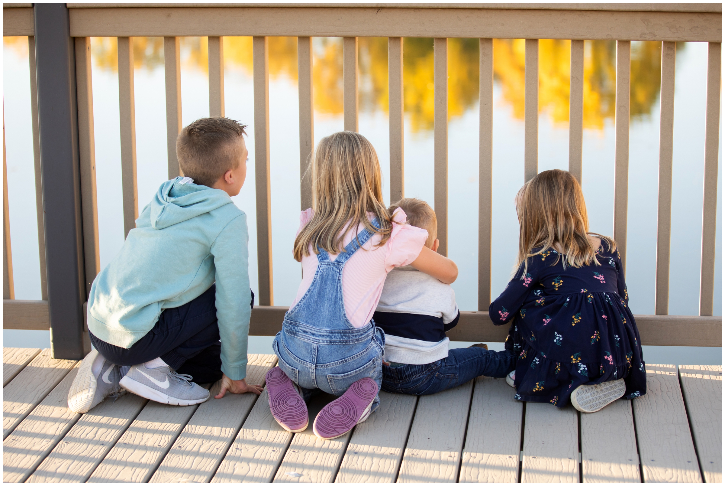 siblings sitting on dock of a lake during fall family photos in Northern Colorado by Plum Pretty Photography 