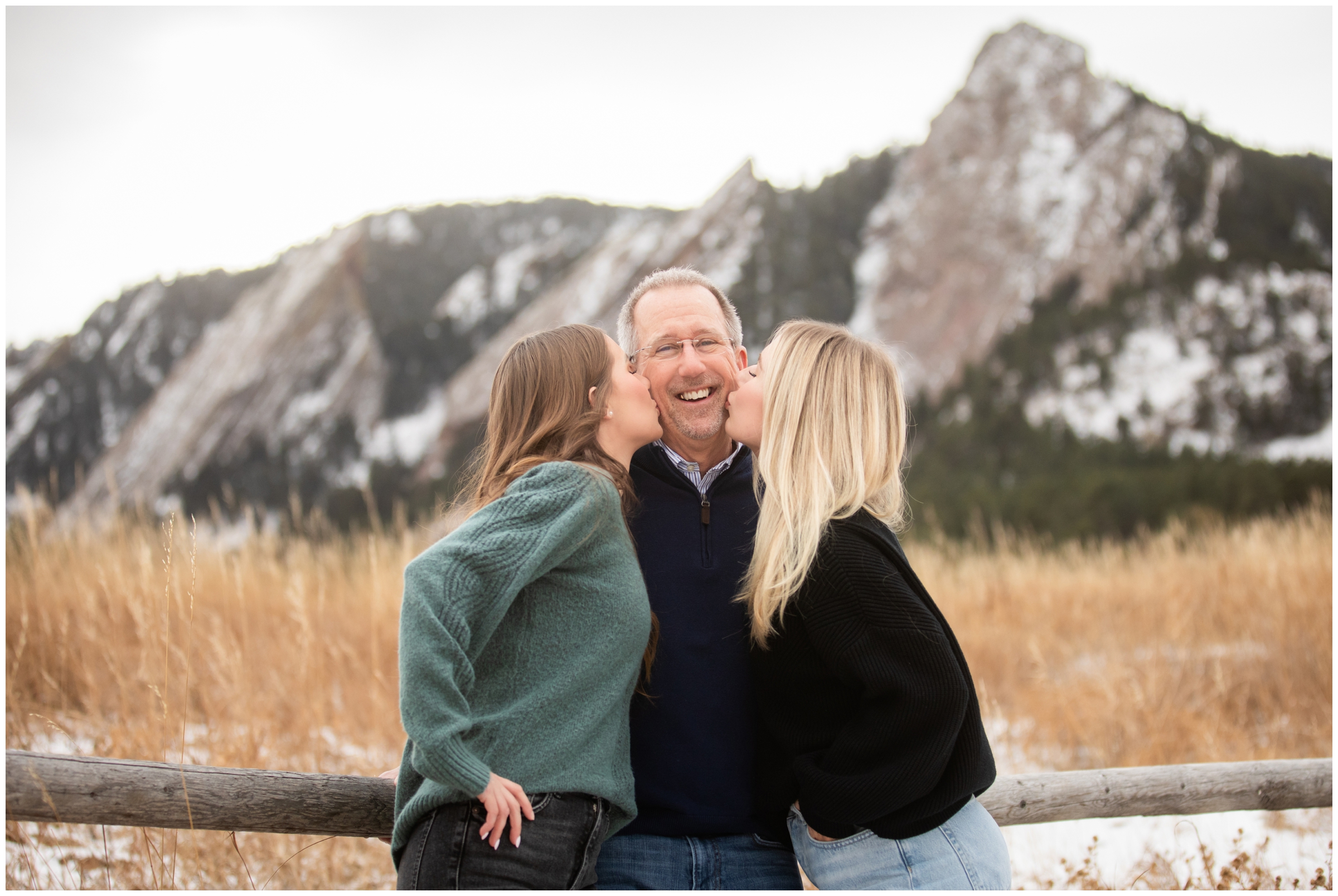 daughters kissing dad's cheeks with mountains in background during winter family photos in Boulder Colorado 