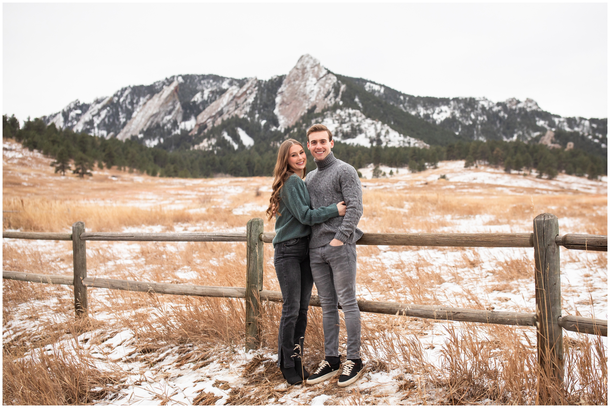 couple cuddling against fence with flatirons in background during Colorado couple's portraits at Chautauqua Park 