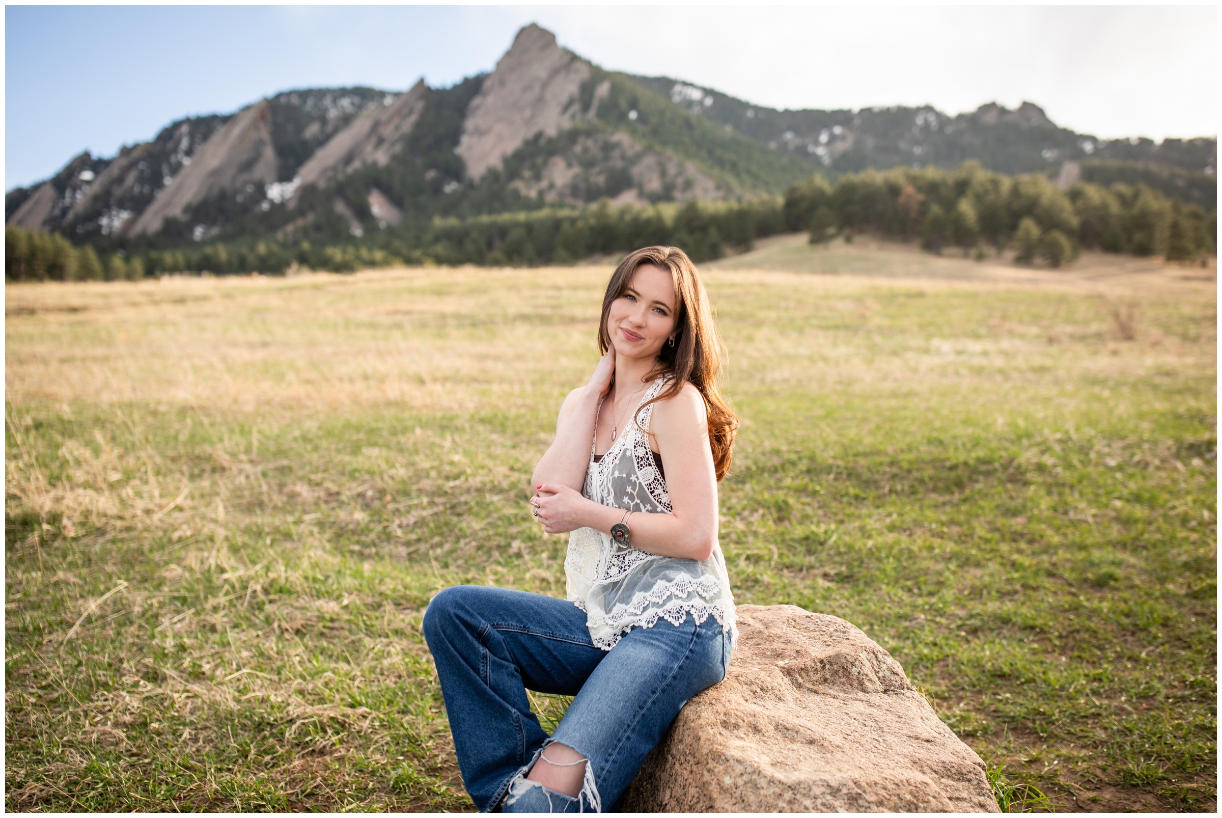 woman sitting on rock with flatirons in background during CU Boulder college senior pictures at Chautauqua