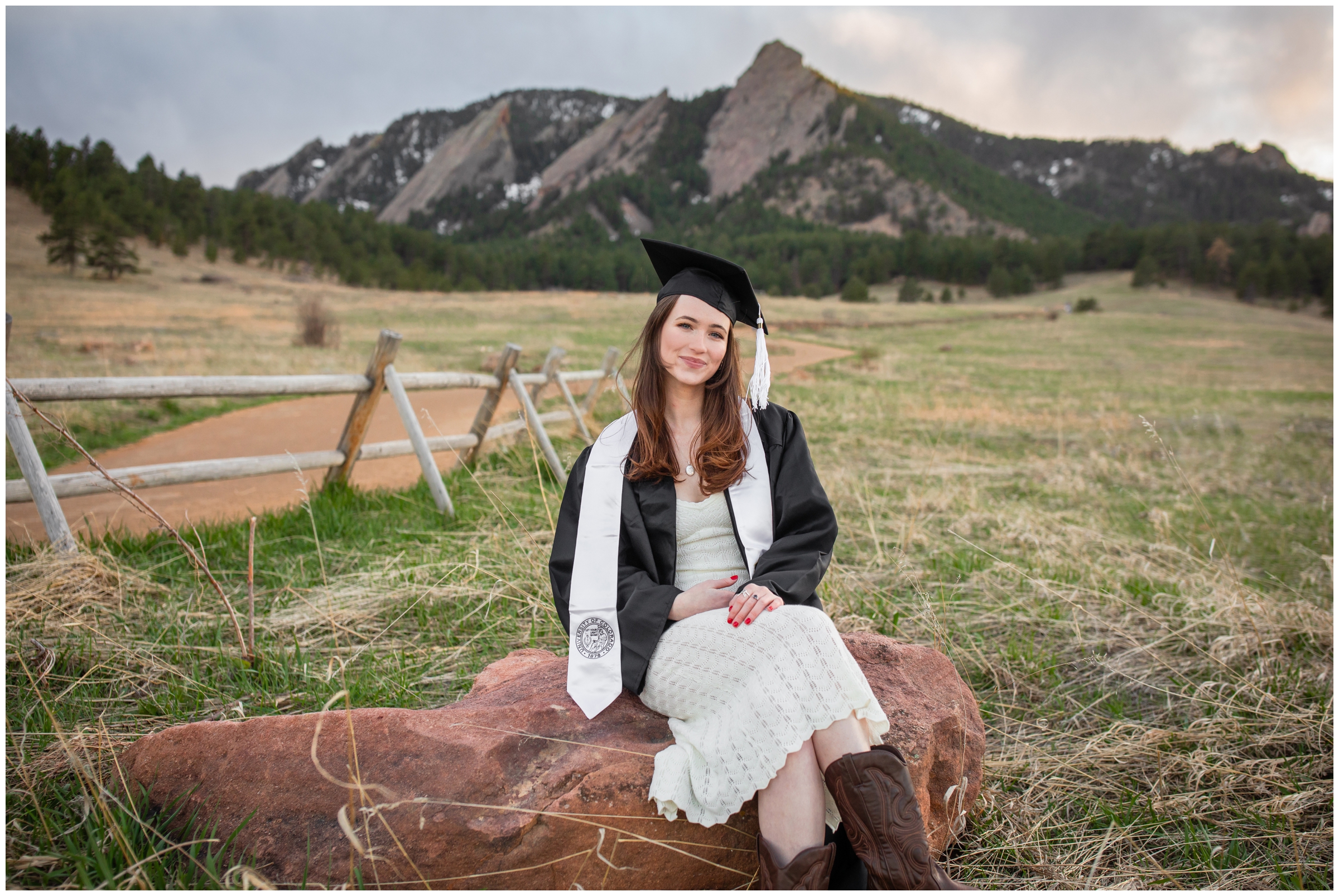 woman sitting on a rock in her cap and gown during college senior pictures in Boulder Colorado